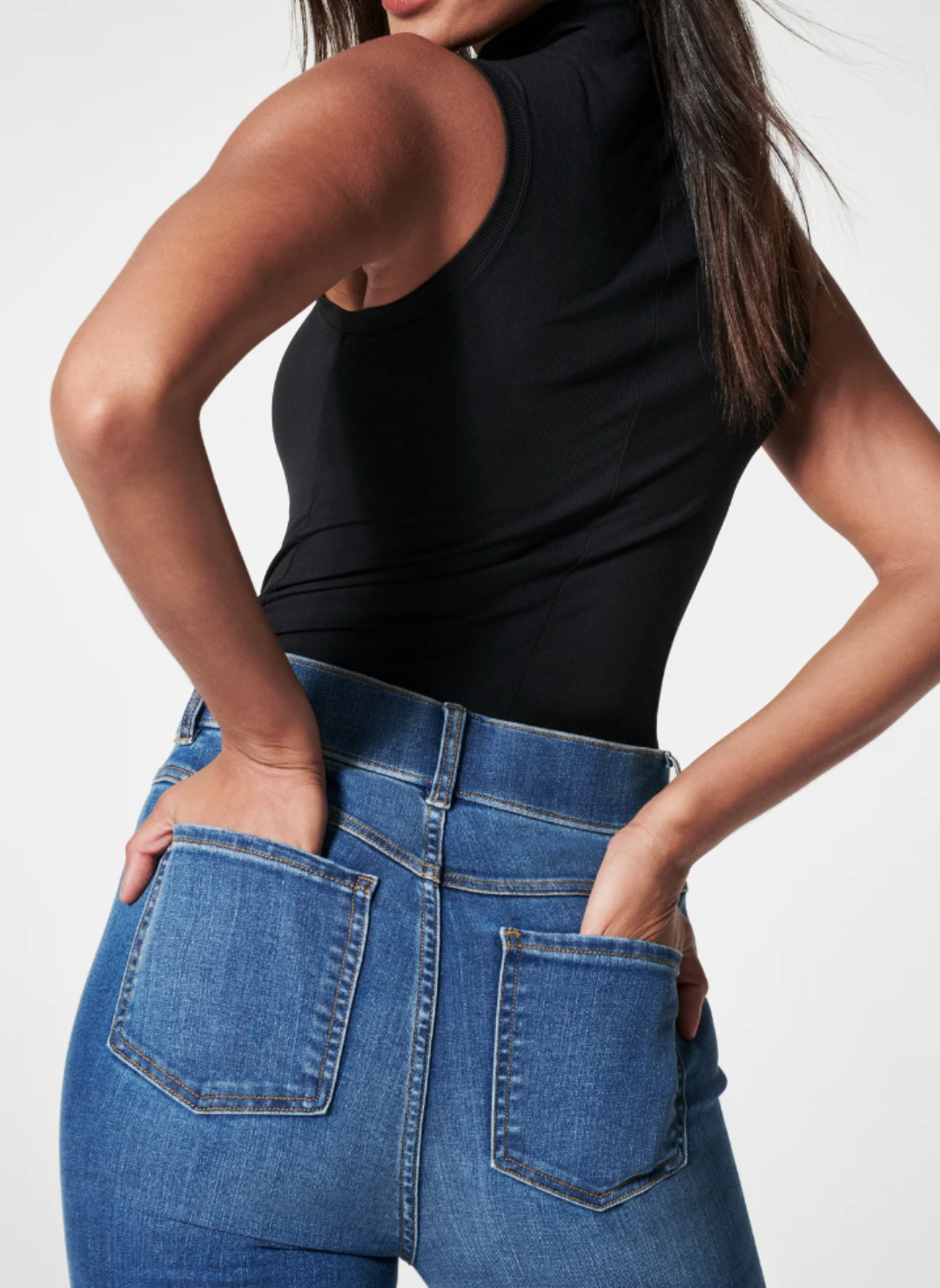 Back view of the model wearing the SPANX Ocean Flare Jeans showing the back pockets with her hands in it.
