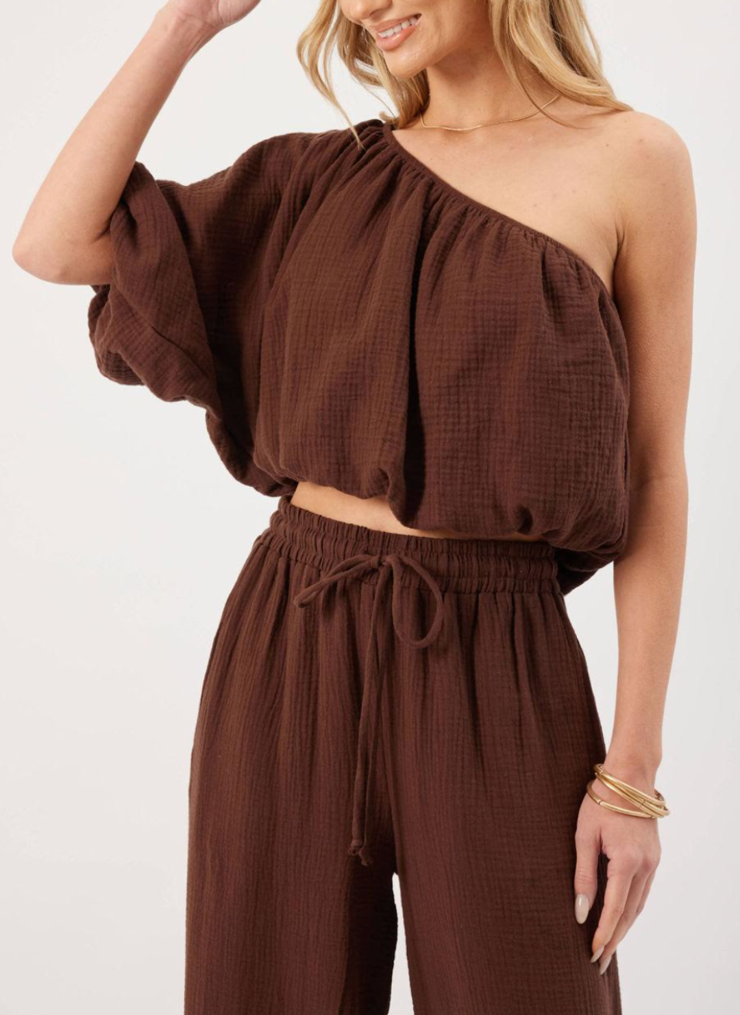 Model wearing brown KP Lina Top with one shoulder detail and bubble hem along with matching pants.