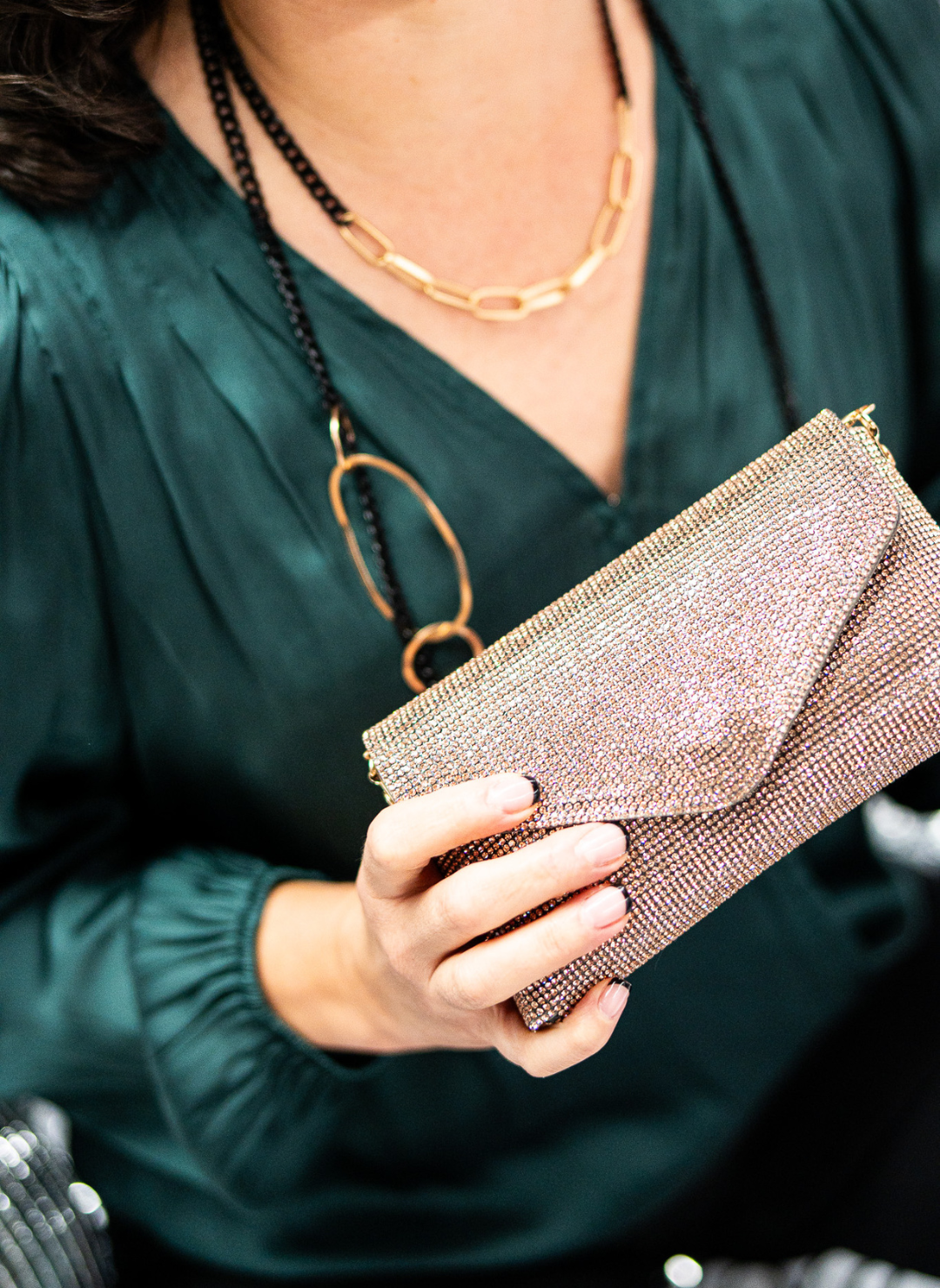 Close up view if model wearing black chain infinity necklace paired with rose gold glitter clutch purse.