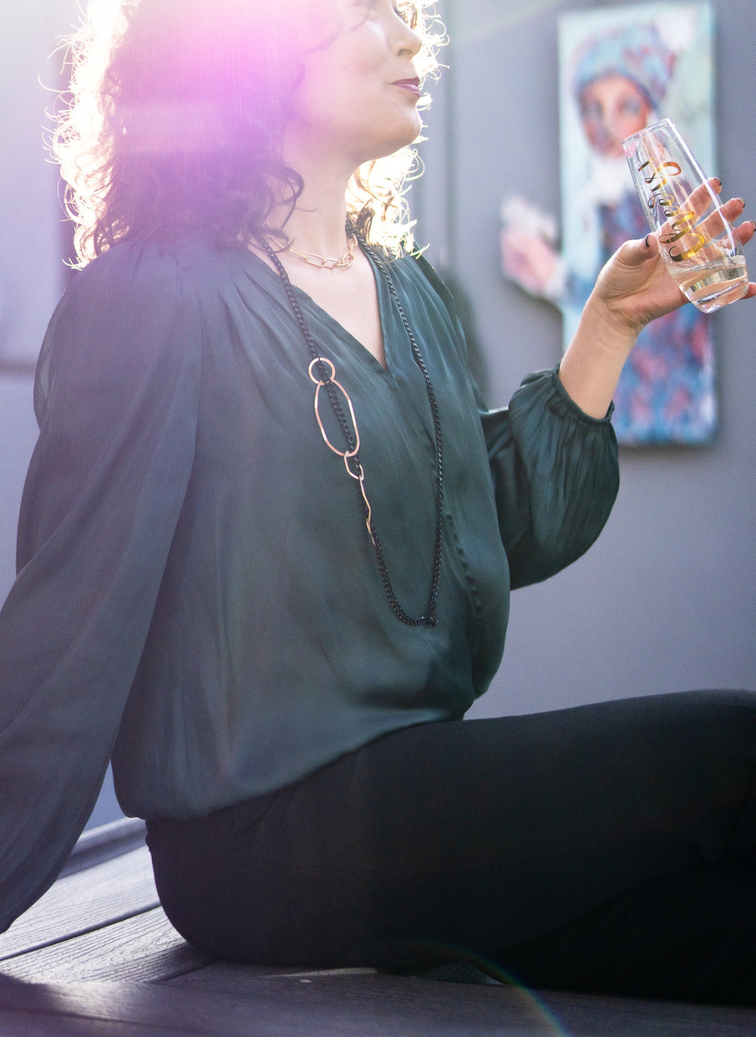 Model is sitting wearing a black chain necklace with a dark green top.