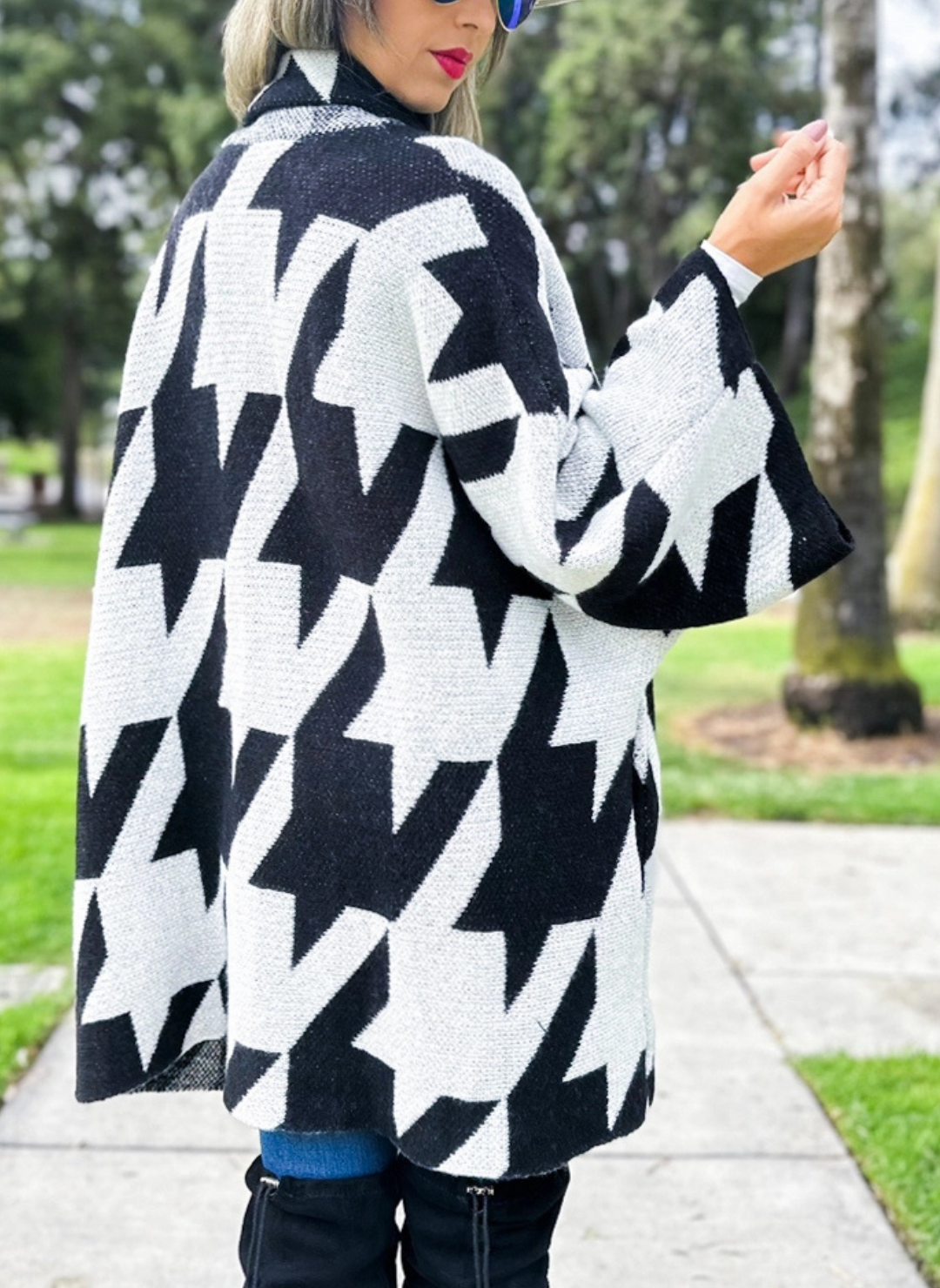 Full back view of model wearing the Houndstooth Oversized Cardi paired with denim bottoms and black boots. Model is standing outside.