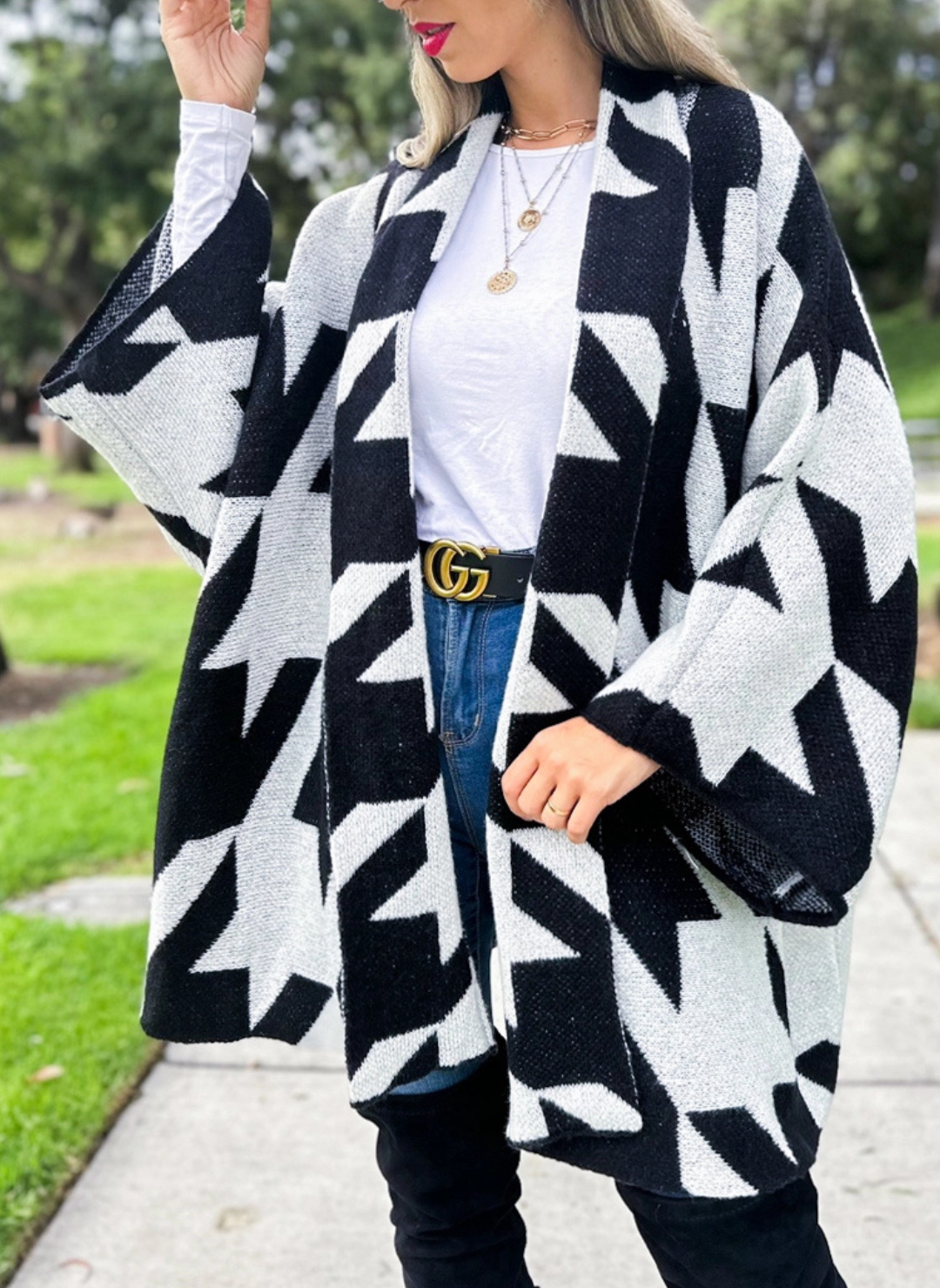Full front view of model wearing the Houndstooth Oversized Cardi paired with a white top, denim bottoms, and black boots. Model is standing outside.