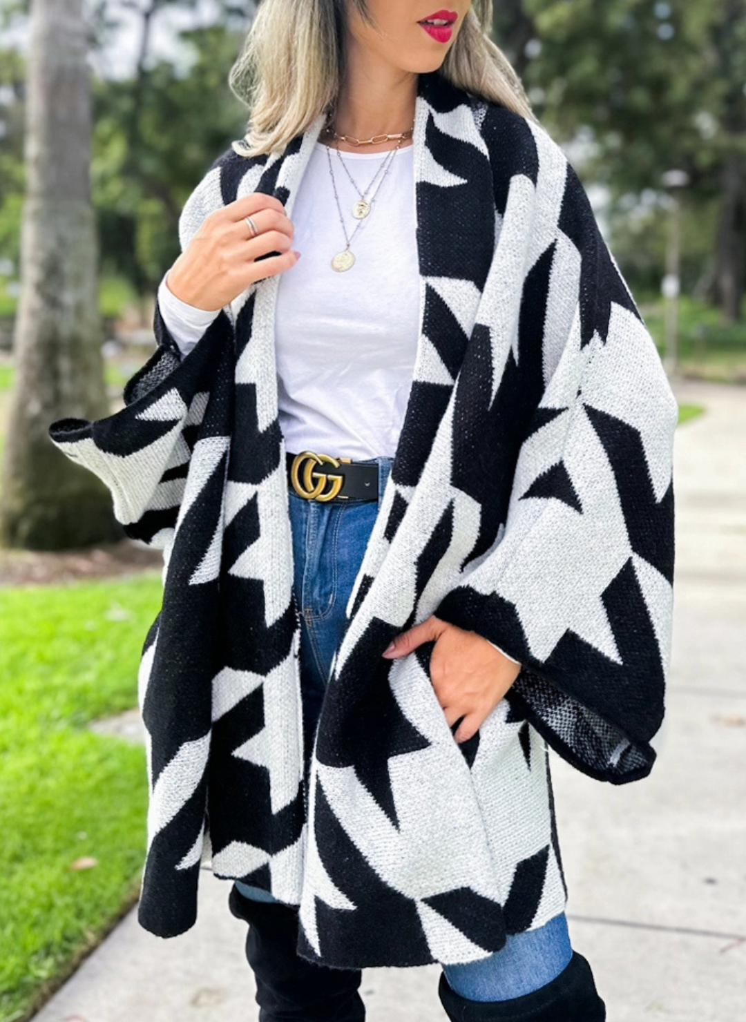 Full front view of model wearing the Houndstooth Oversized Cardi paired with a white top, denim bottoms, and black boots. Model is standing outside.