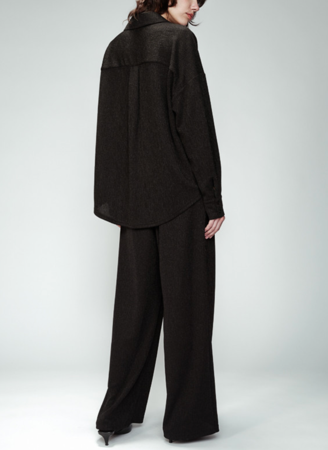 Back view of the model wearing the Grace & Mika Olympe Button Down Shirt paired with black pants. Model is standing in front of white background.