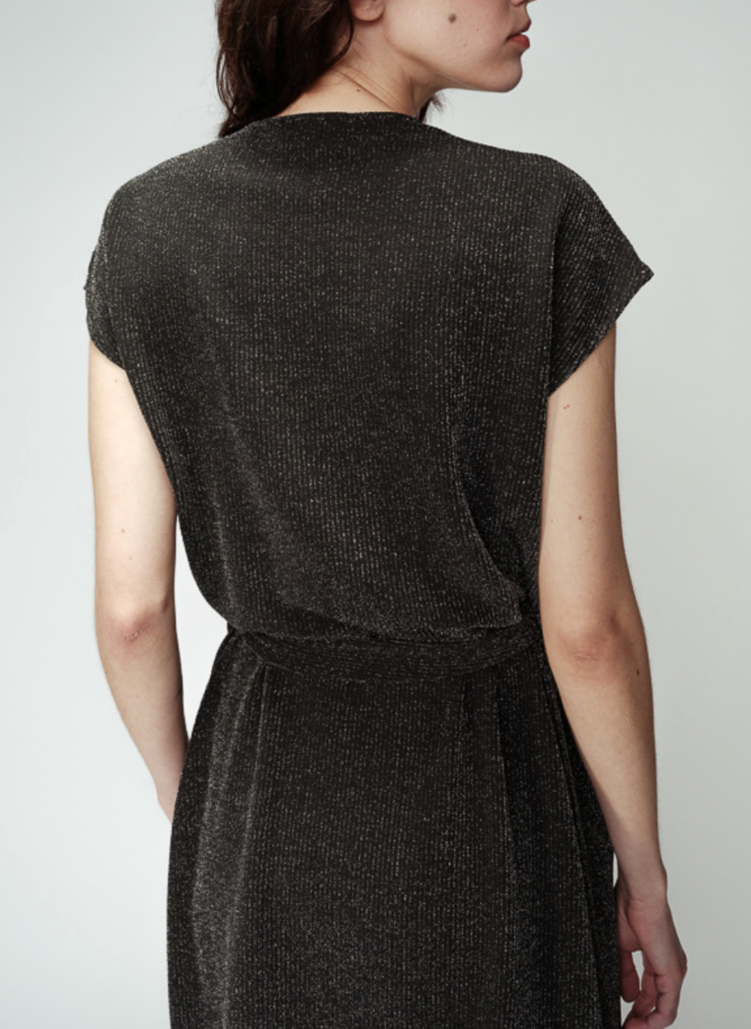 Back view of Bright Lights Belted Dress. Subtle shimmer stripes are running through the material of the dress. Models arms are by her side. White background.