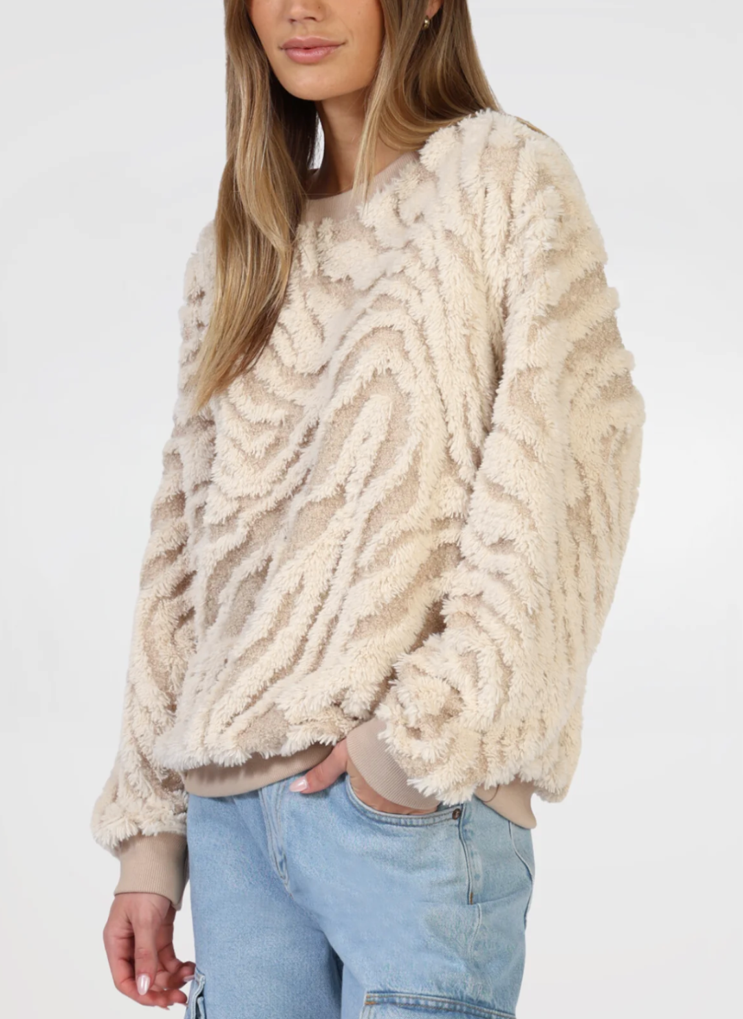 Model is wearing tan and cream sweater. Models right hand is in pocket, portraying a closer view of the sweaters textured detail.