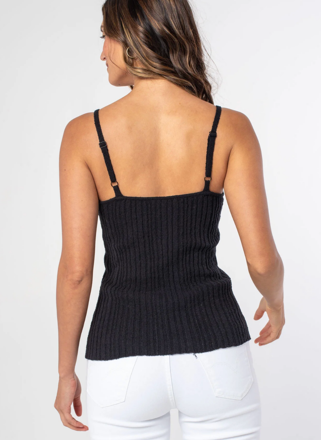 Back view of model wearing the Sheena Sweater Knit Rib Tank paired with white pants. Model is standing informs of white background.