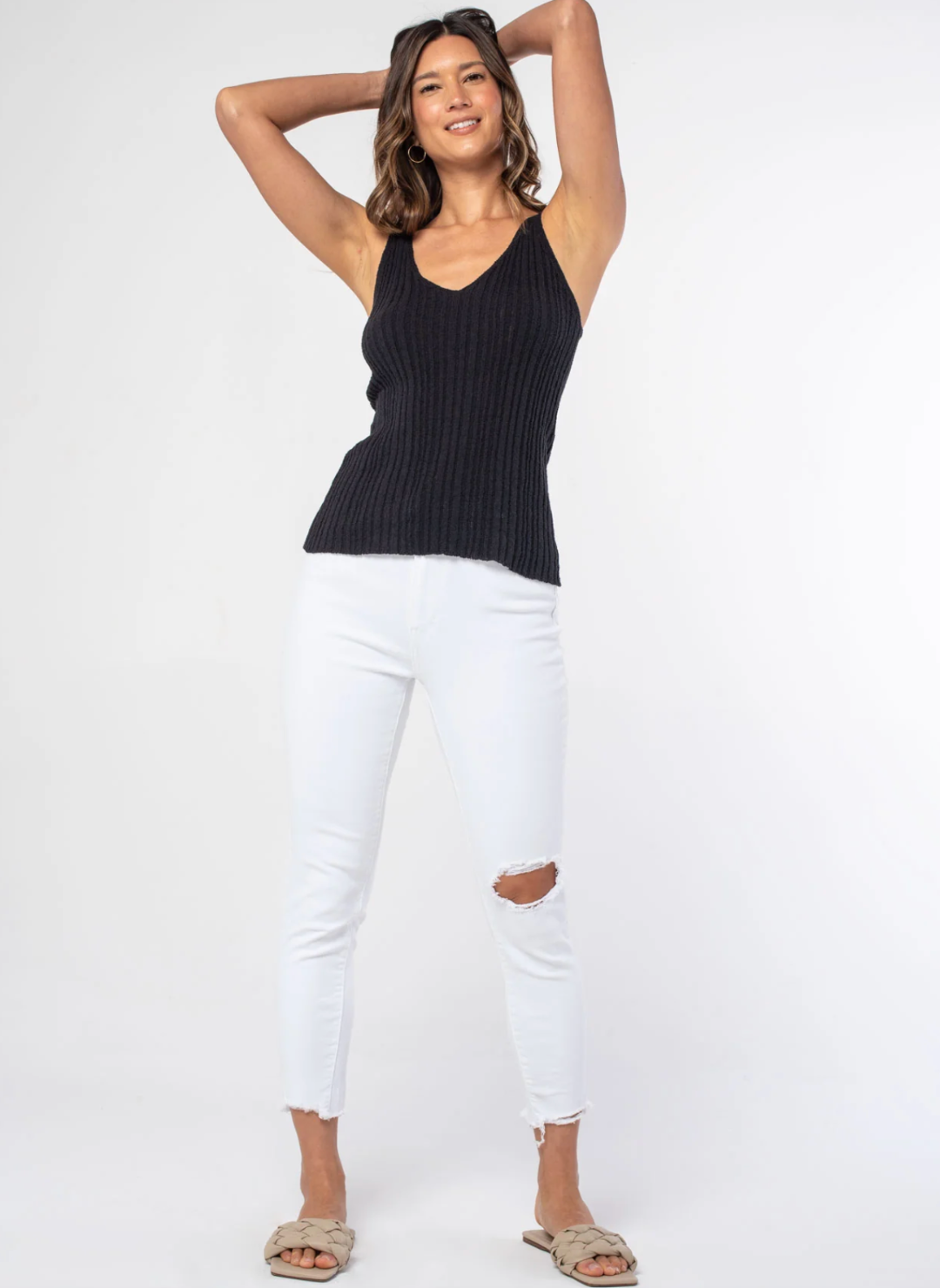 Front view of model wearing the Sheena Sweater Knit Rib Tank paired with white pants and tan sandals. Model is standing informs of white background.