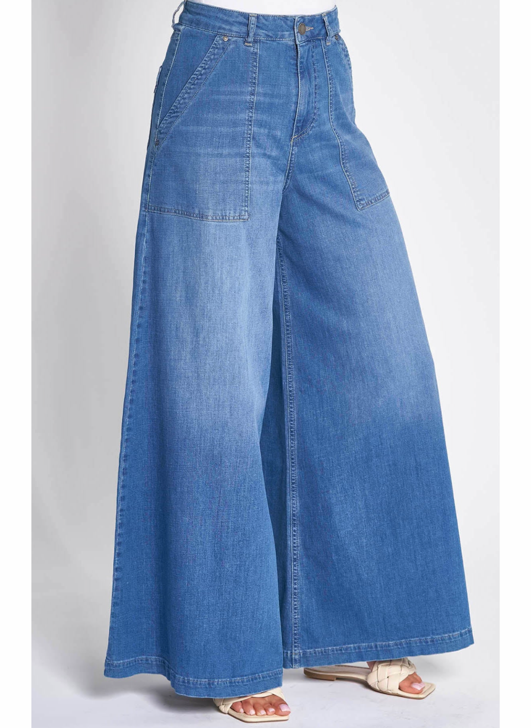 Full front/side view of model wearing  the ZHrill Chatti Wide Leg Denim pant paired with a white top and white sandals. Model is standing in front of a white background.