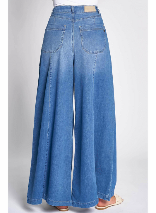 Full back view of model wearing  the ZHrill Chatti Wide Leg Denim pant paired with a white top and white sandals. Model is standing in front of a white background.