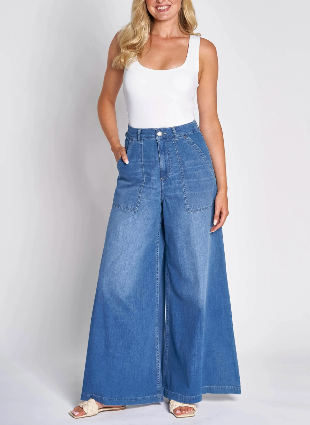 Full front view of model wearing  the ZHrill Chatti Wide Leg Denim pant paired with a white top and white sandals. Model is standing in front of a white background.