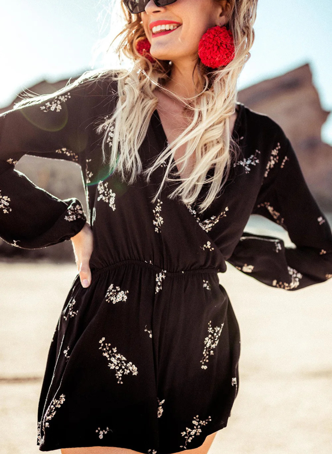 Woman wearing a black floral romper with long sleeves, surplice wrap front, and elastic waist—lightweight, flattering, and perfect for spring events, date nights, or travel.