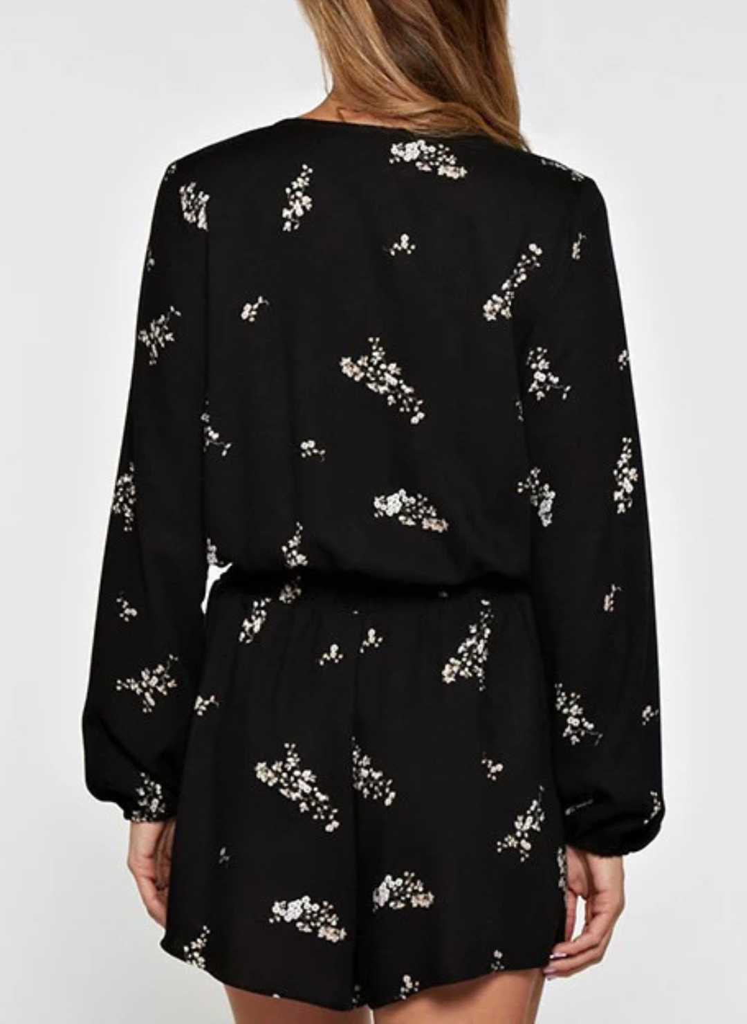 Back view of a woman wearing a black floral romper with long sleeves, surplice wrap front, and elastic waist—lightweight, flattering, and perfect for spring events, date nights, or travel.