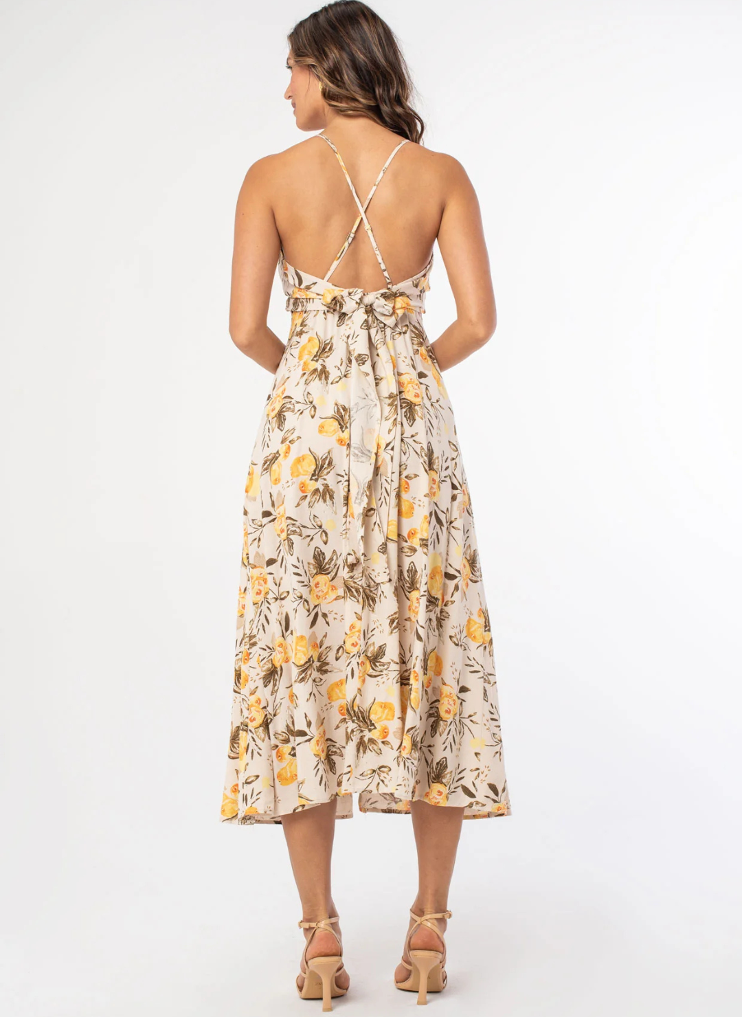 Back view of a woman wearing a lemon print midi dress with adjustable crisscross straps, surplice neckline, and tie-back bow detail—lightweight fabric and A-line silhouette perfect for warm weather.