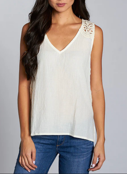 Woman wearing a sleeveless ivory tank top with intricate crochet lace detailing on the shoulders and upper back. The Lovestitch Crochet Tank features a soft cotton gauze front, knit jersey back, and relaxed boho-inspired fit—perfect for boutique-style summer outfits.