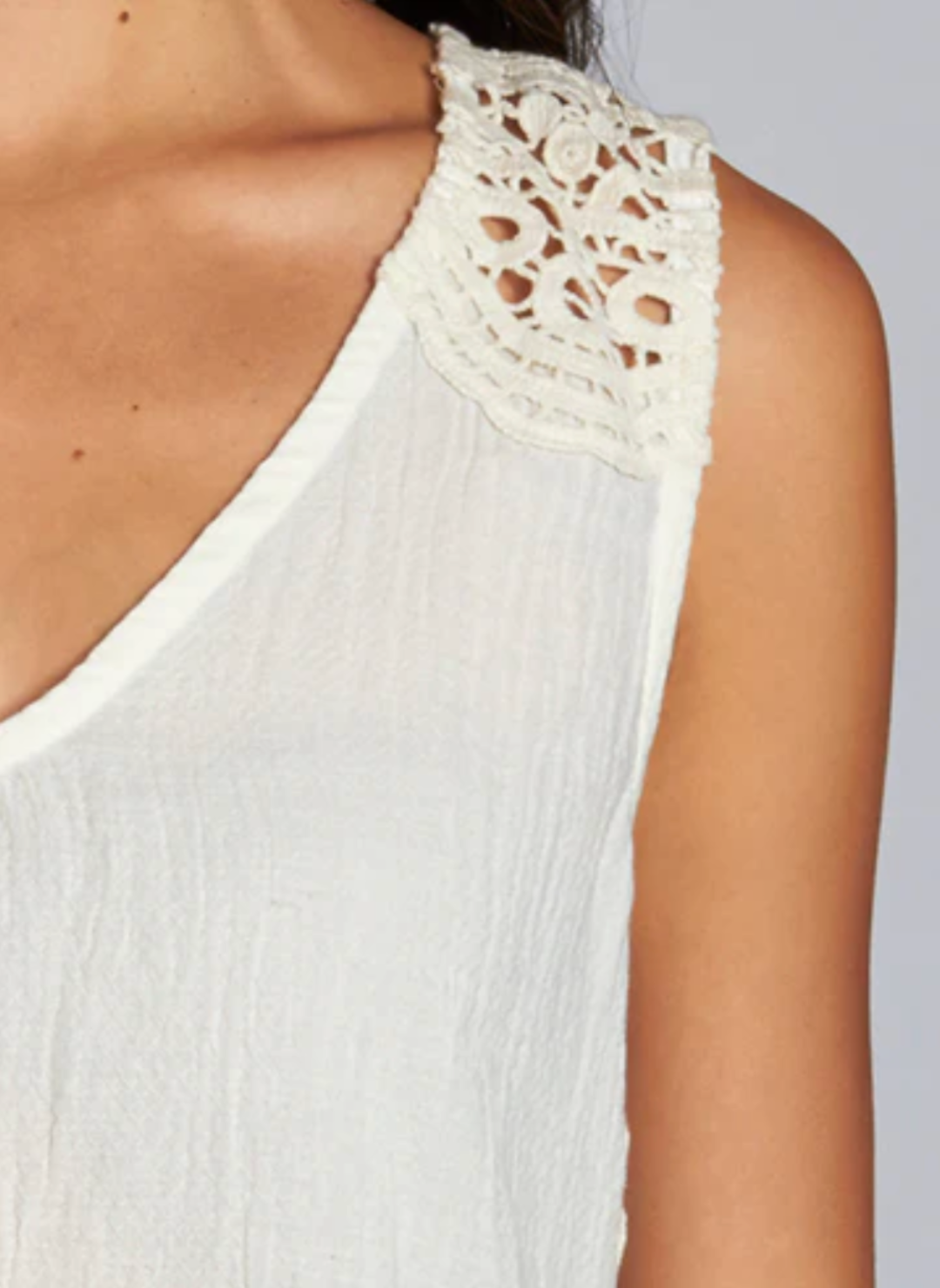 Woman wearing a sleeveless ivory tank top with intricate crochet lace detailing on the shoulders and upper back. The Lovestitch Crochet Tank features a soft cotton gauze front, knit jersey back, and relaxed boho-inspired fit—perfect for boutique-style summer outfits.