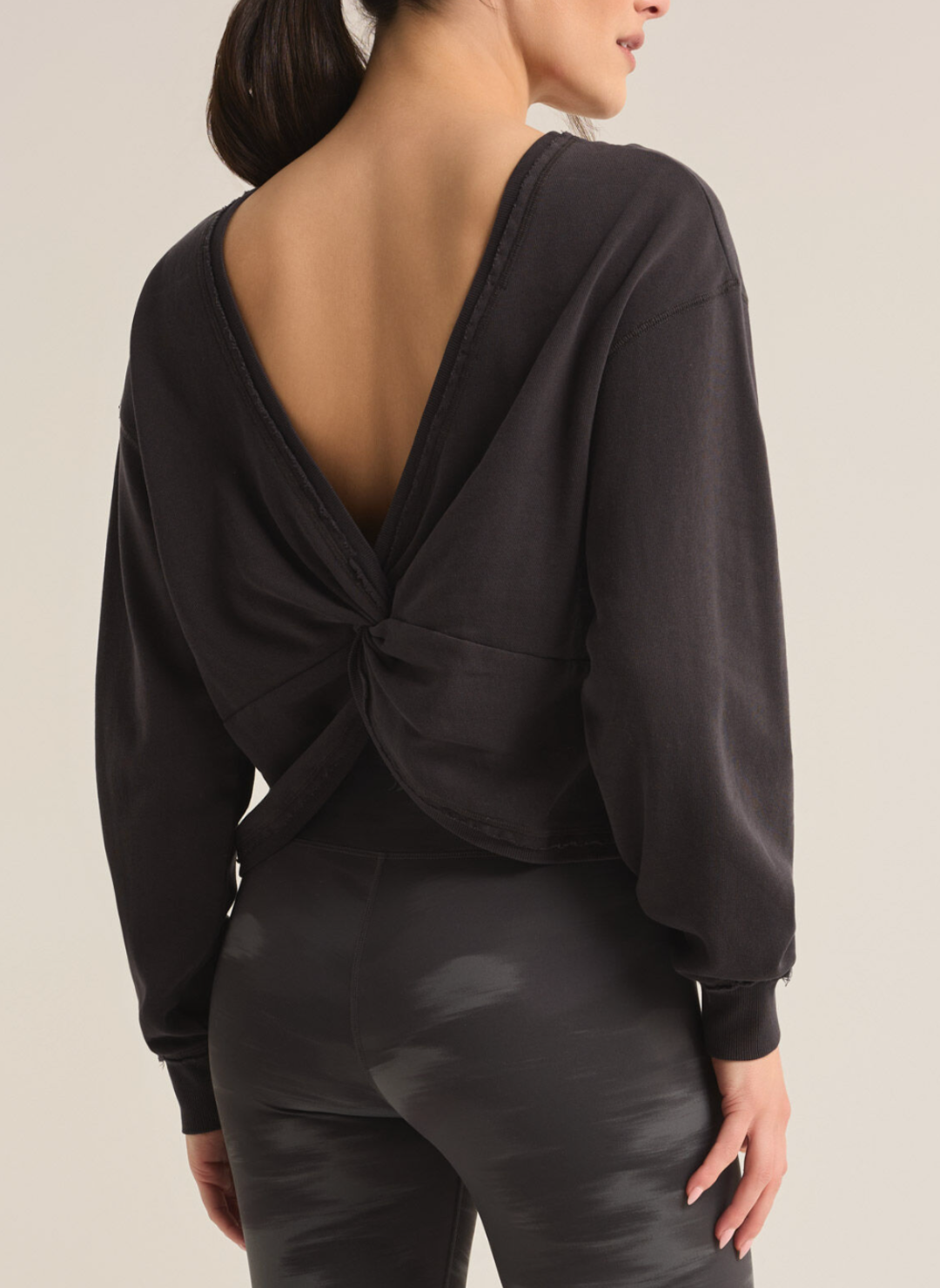 Model is wearing Rita Reversible twist sweatshirt in black. The back of the sweatshirt is showed to display the twisted back.