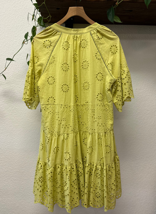 Yellow dress with floral patterns on a hanger against a neutral wall.