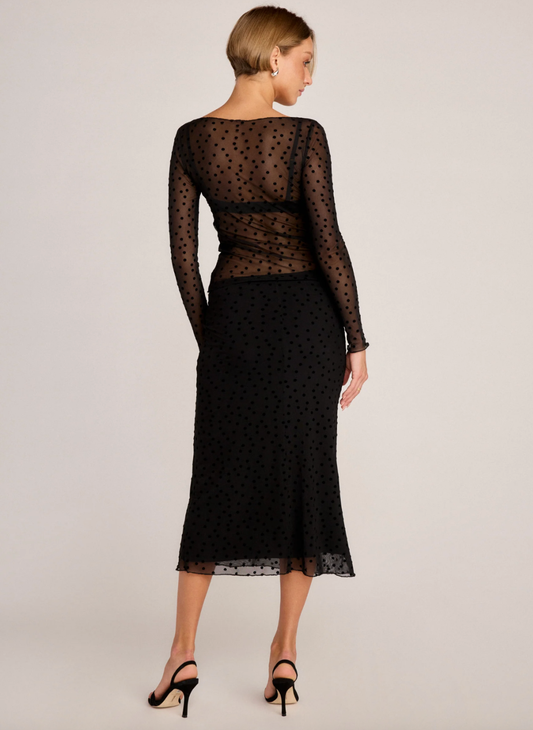 Woman wearing a long sleeve black lace polka dot top & matching skirt on a light gray background