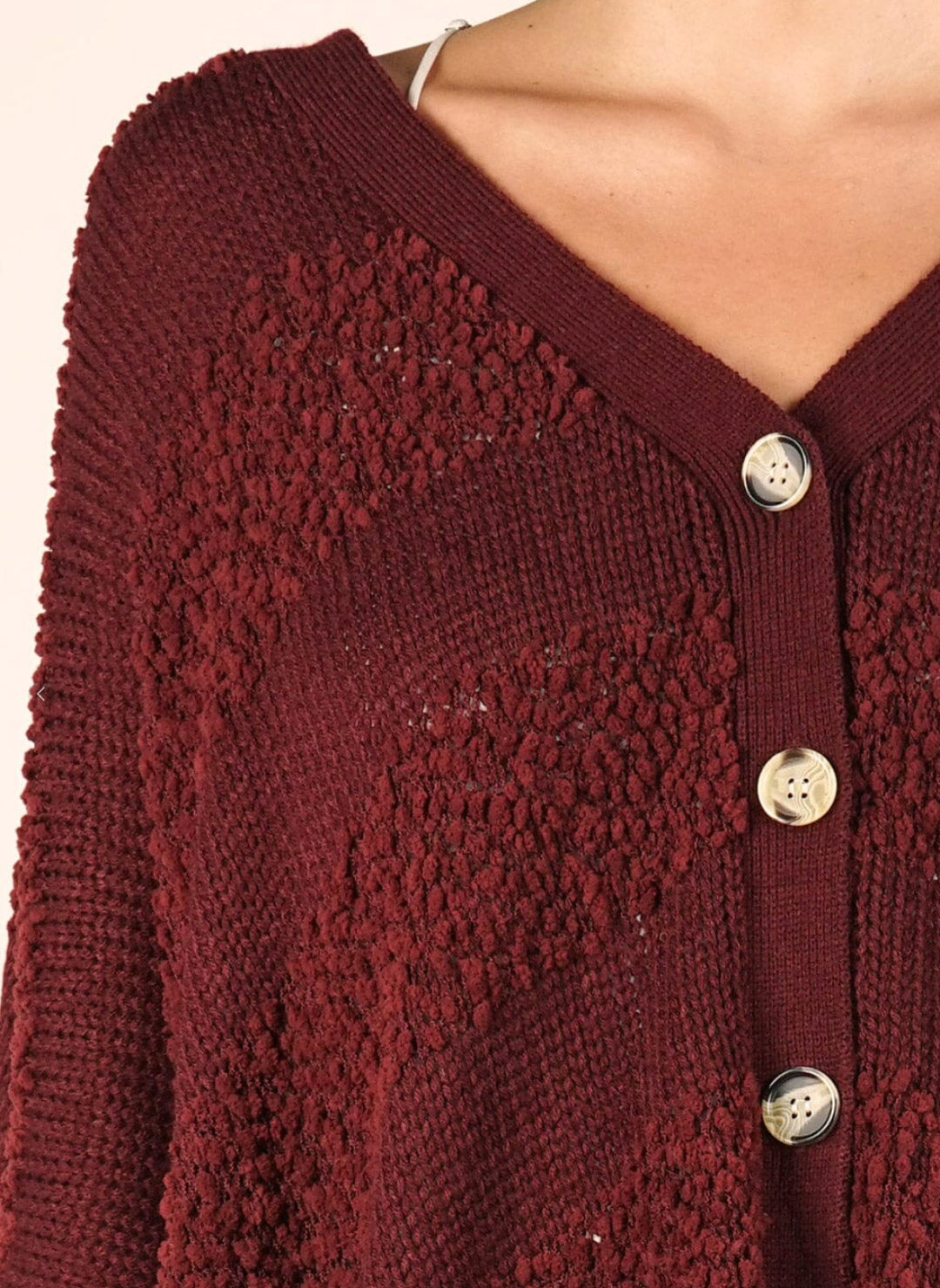 Close-up of a maroon cardigan with button details on a neutral background