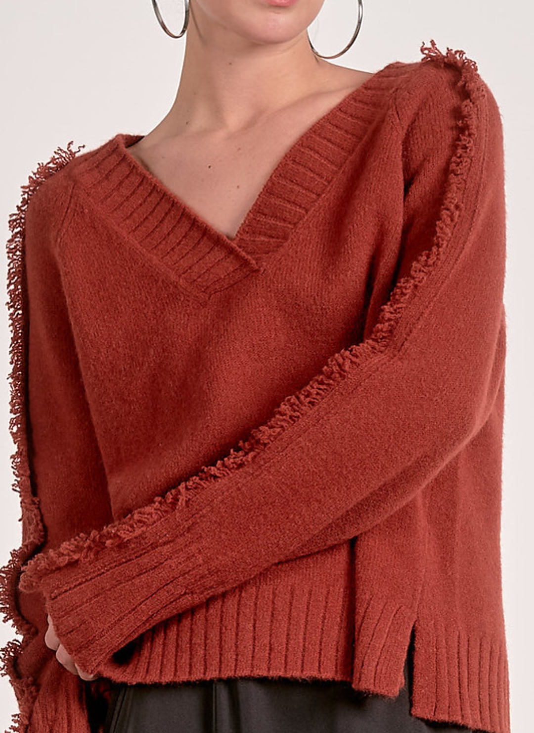 Model wearing Elan Falling Sweater in rust with fringe trim along sleeves and shoulders.
