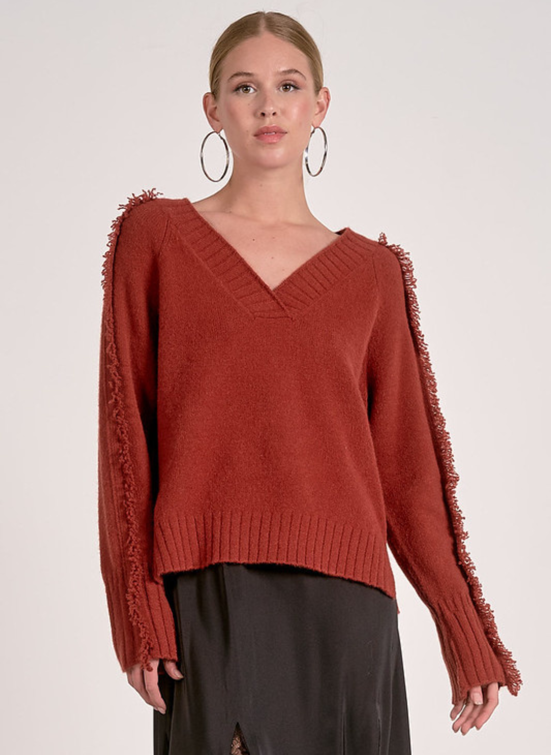 Model wearing Elan Falling Sweater in rust with fringe trim along sleeves and shoulders.