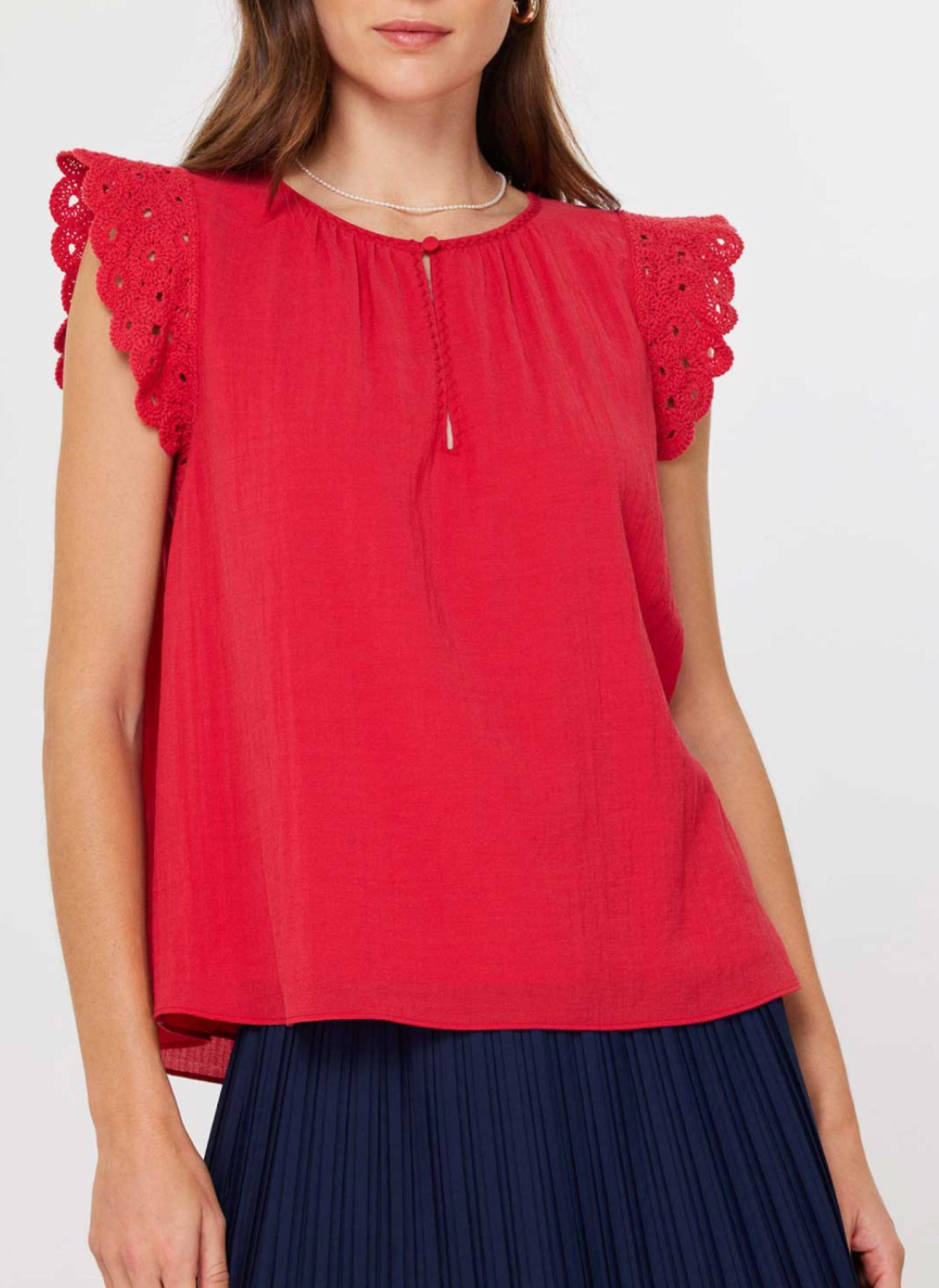 Front and back views of the Current Air Fire Fly Top: a ruby red cotton gauze blouse with scalloped crochet flutter sleeves, keyhole button closure at the round neckline, and soft gathers at the yoke, modeled with a pleated navy skirt.