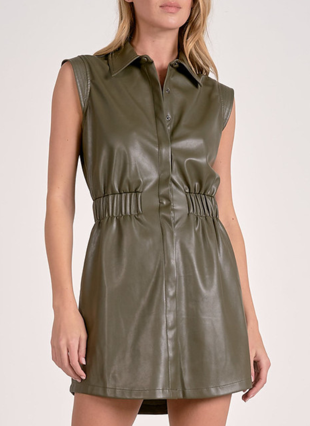 A model with blonde hair wears the Elan "Party Time, Excellent" sleeveless faux leather shirtdress in olive green, showing its collared neckline and cinched elastic waist.