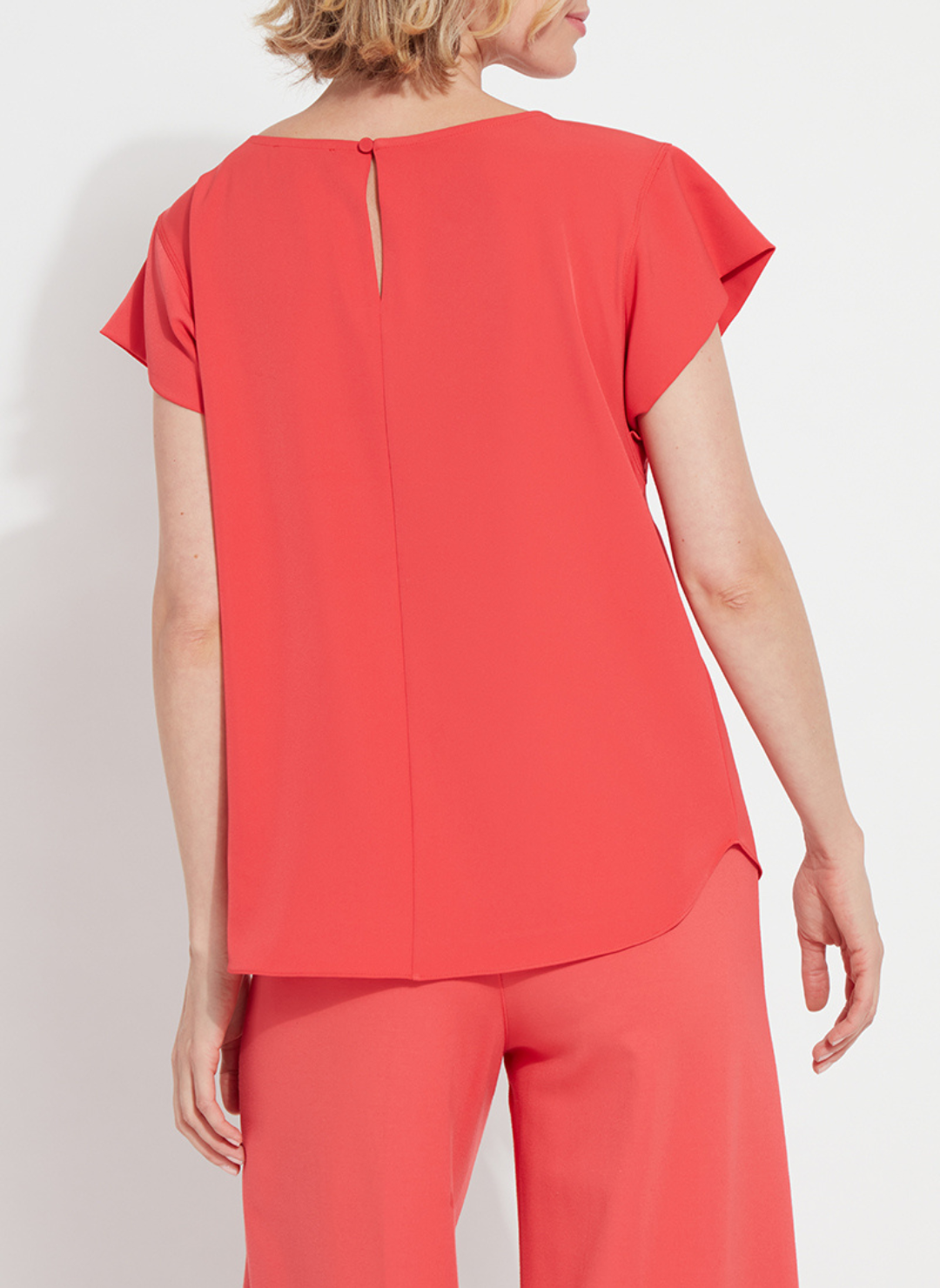 Woman wearing the Melodie Top in Coral Bloom from August Boutique Ripon; features flutter sleeves, scoop neckline, flowy drape, and keyhole back detail. Lightweight and perfect for warm-weather styling.
