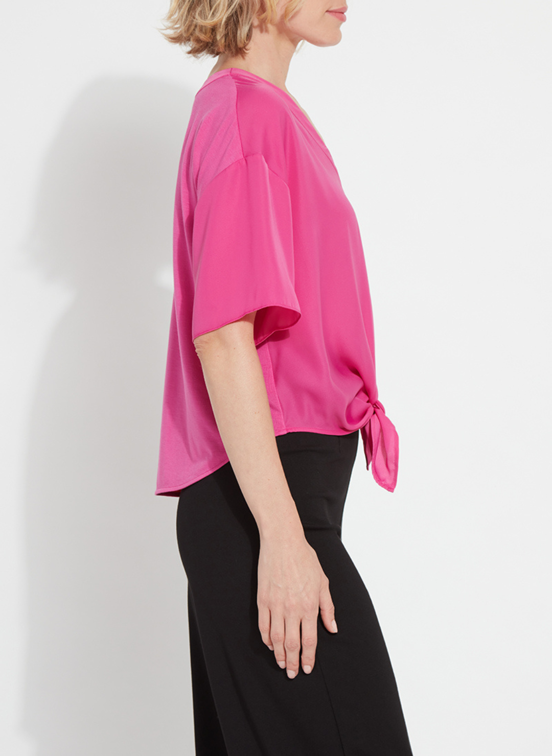 Woman wearing the Lyssé Cleo Tie Up Top in vibrant hot pink; features dolman short sleeves, v-neckline, and tie-front hem. Styled for comfort and polish, available at August Boutique Ripon.