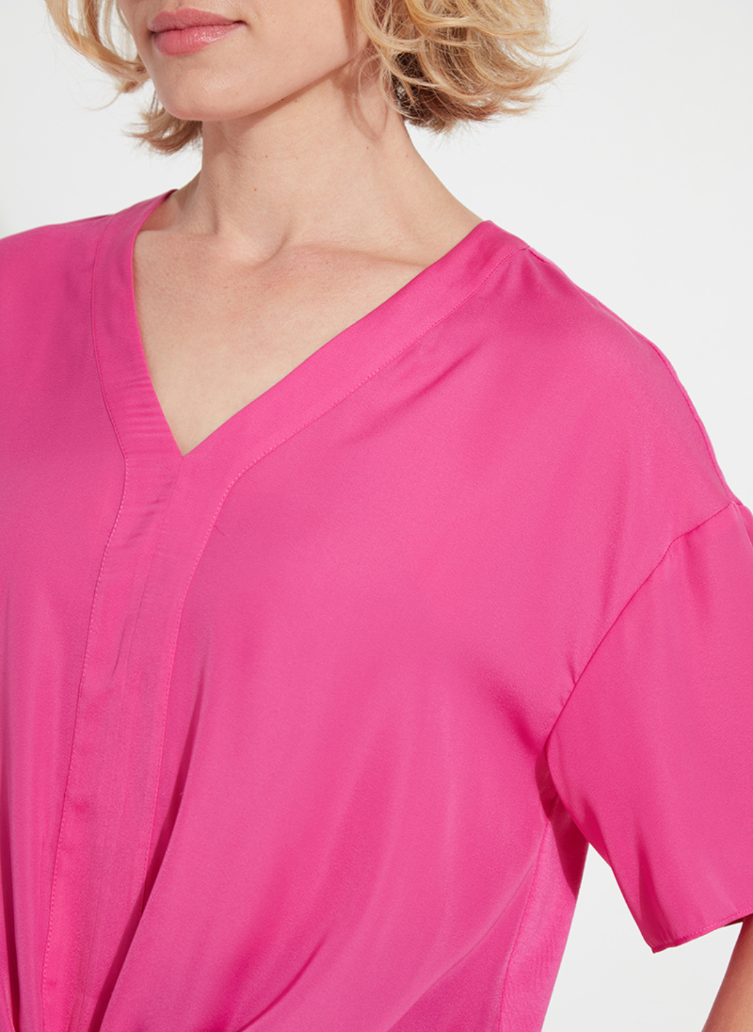 Woman wearing the Lyssé Cleo Tie Up Top in vibrant hot pink; features dolman short sleeves, v-neckline, and tie-front hem. Styled for comfort and polish, available at August Boutique Ripon.