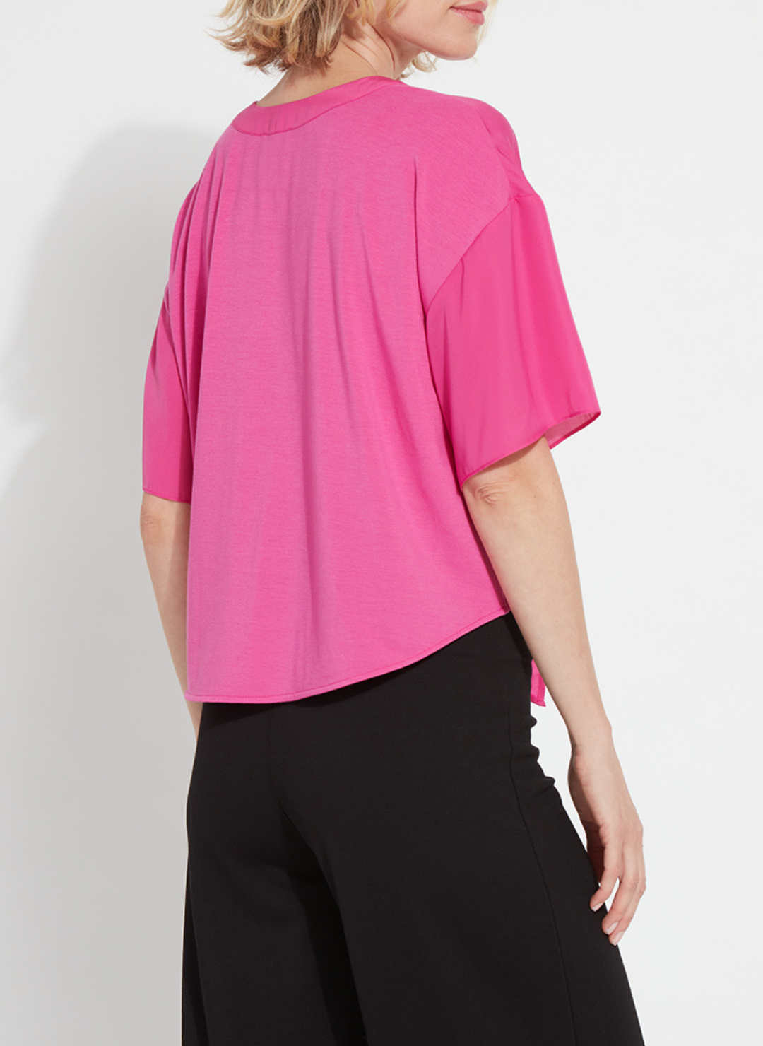 Back view of a woman wearing the Lyssé Cleo Tie Up Top in vibrant hot pink; features dolman short sleeves, v-neckline, and tie-front hem. Styled for comfort and polish, available at August Boutique Ripon.