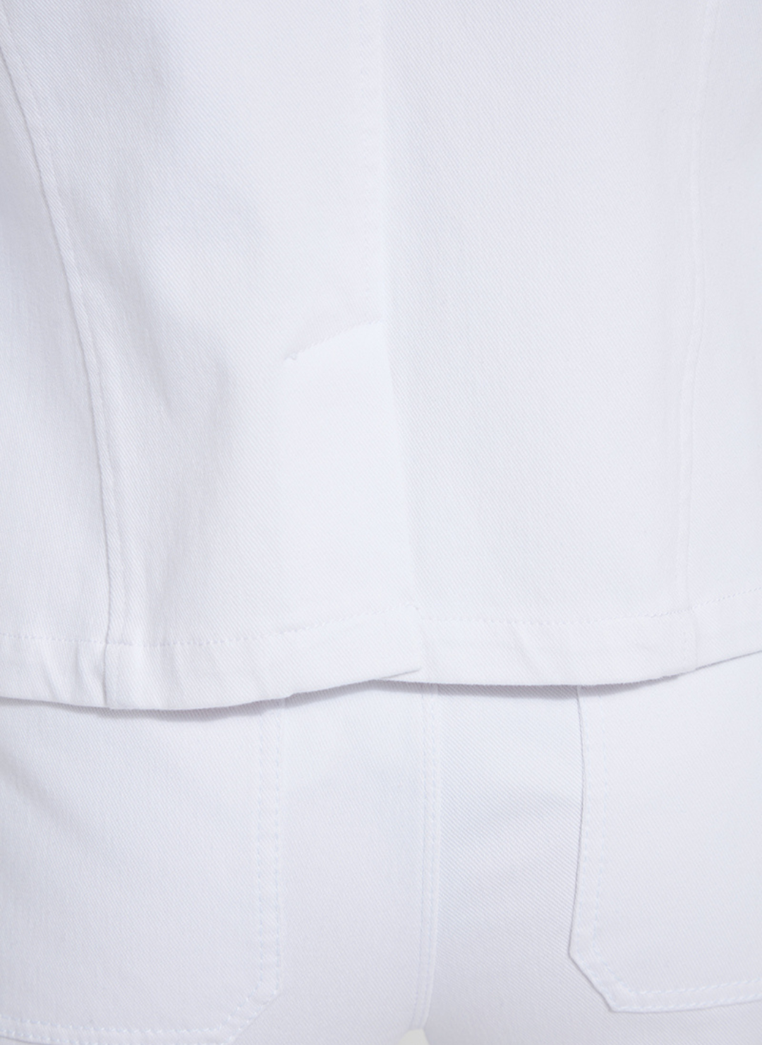 Close up view of the back hem of the white stretch denim blazer by Lyssé.