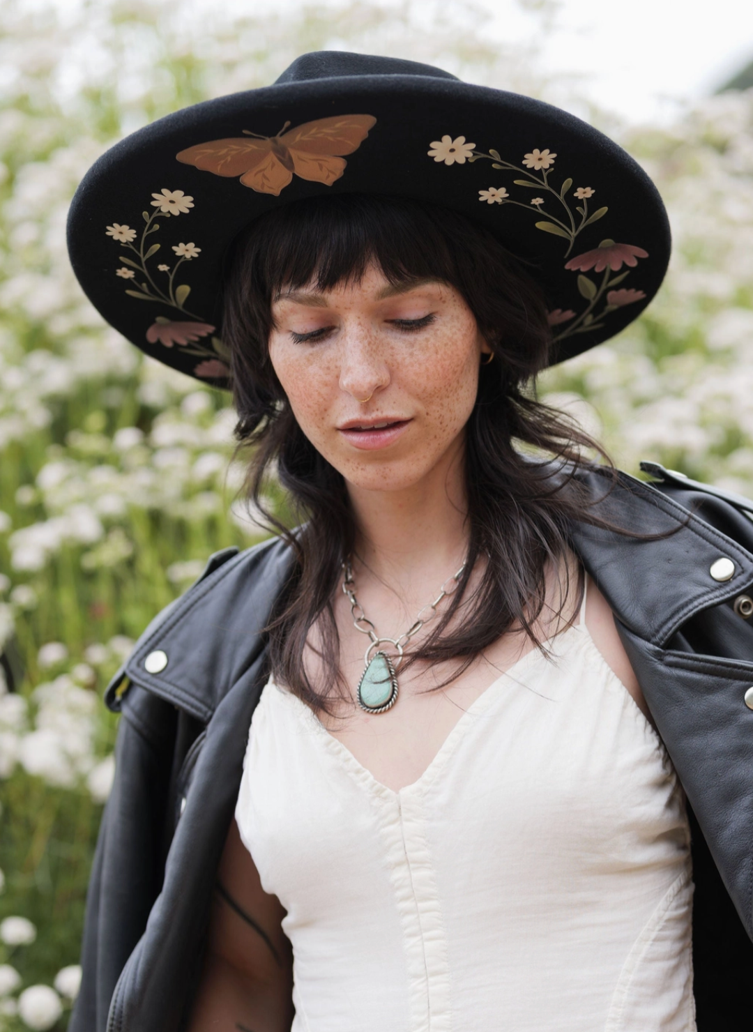 Model wearing black Flutter By Hat with hand drawn florals and butterfly illustrations under the brim.