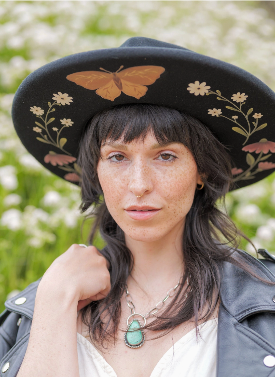 Model wearing black Flutter By Hat with hand drawn florals and butterfly illustrations under the brim.