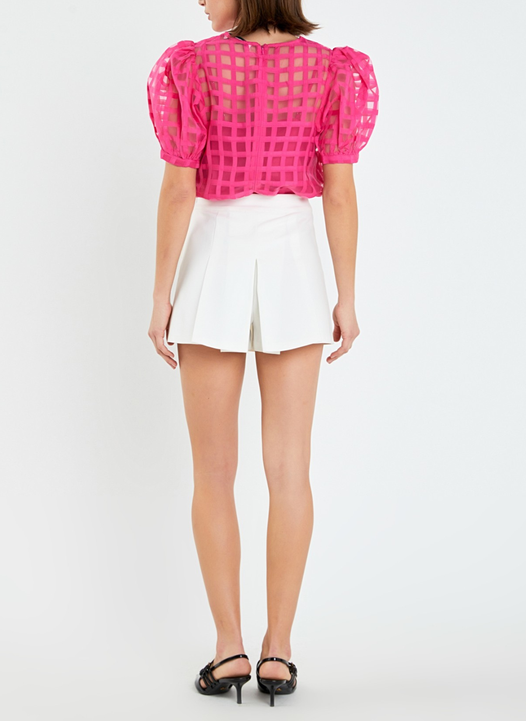 Full body back view of model wearing pink Off the Grid Top with white shorts and black heels.