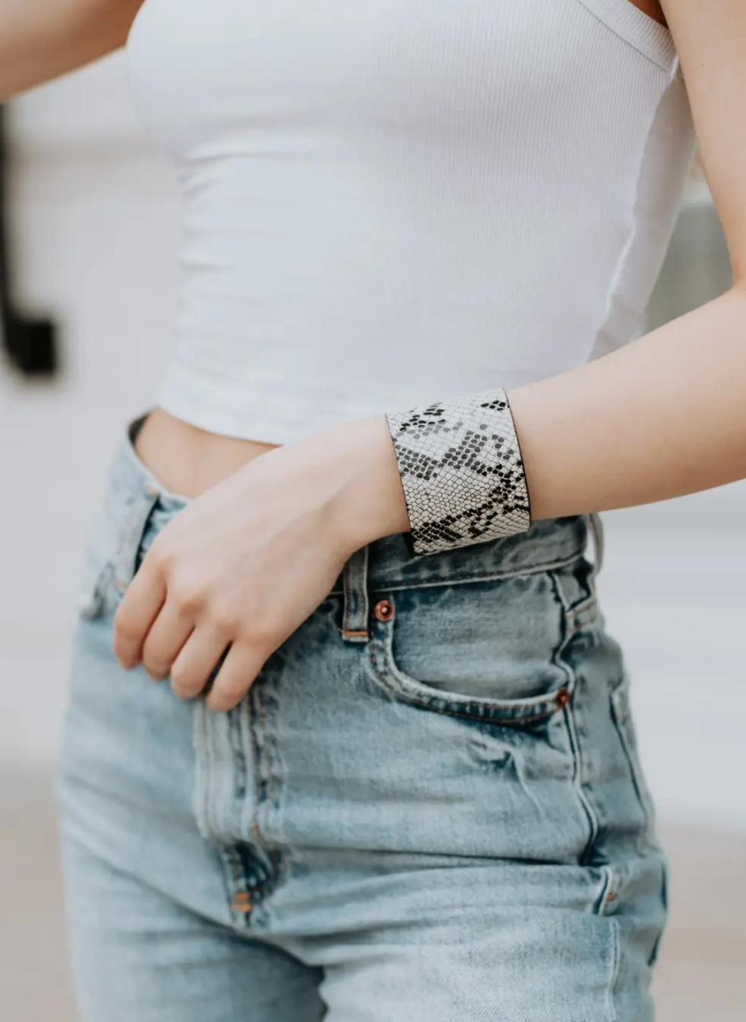 Full view of model wearing Snakeskin Cuff, white top, and denim bottoms. White background.