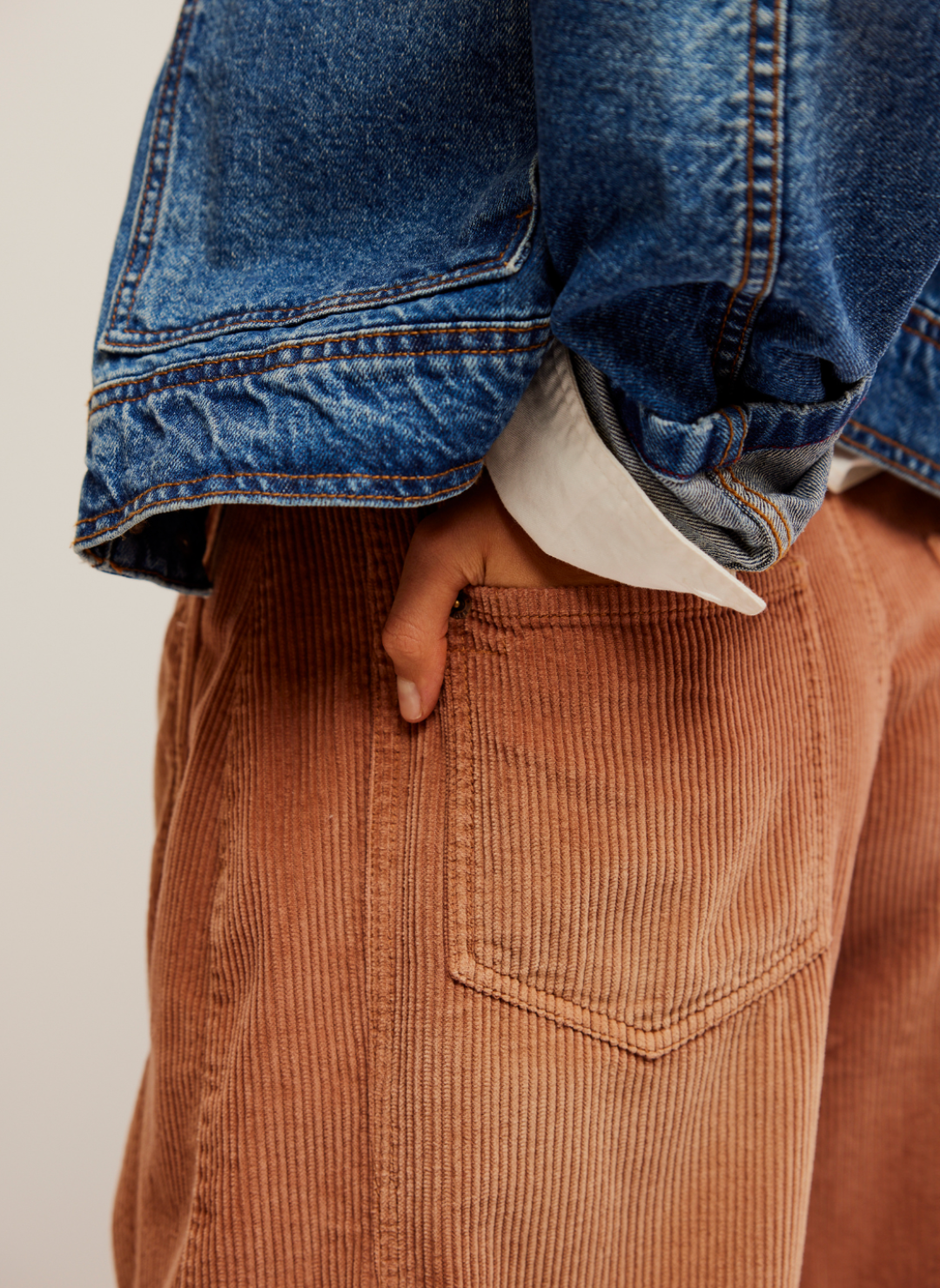 Close up of back pocket with model's hand in it. Jean jacket on top. Rust color corduroy pants.