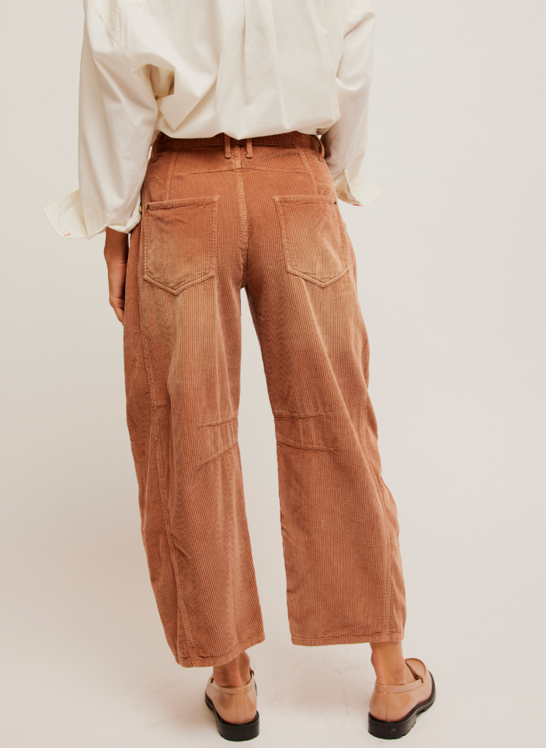 Back View: Pictured a corduroy pant in a rust color.  Darts at the inner knee and a tapered hem.  White shirt paired with it and loafers.