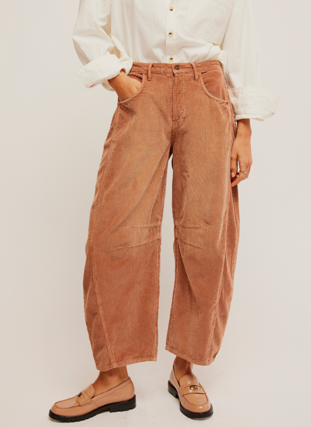 Pictured a corduroy pant in a rust color. Darts at the inner knee and a tapered hem. White shirt paired with it and loafers.