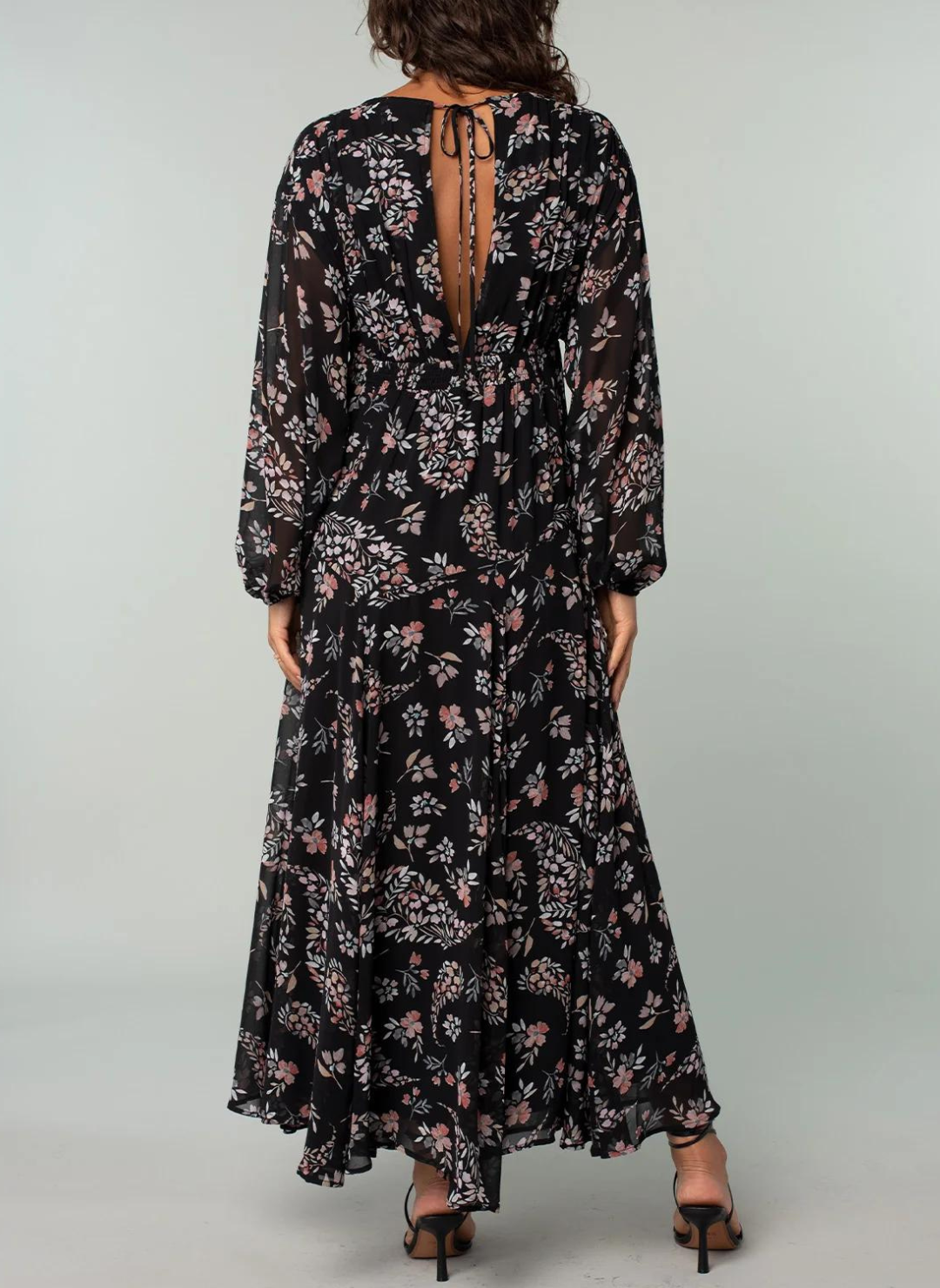 Model is showing the back of the floral dress, where there is a V-neck with a string tie on top.