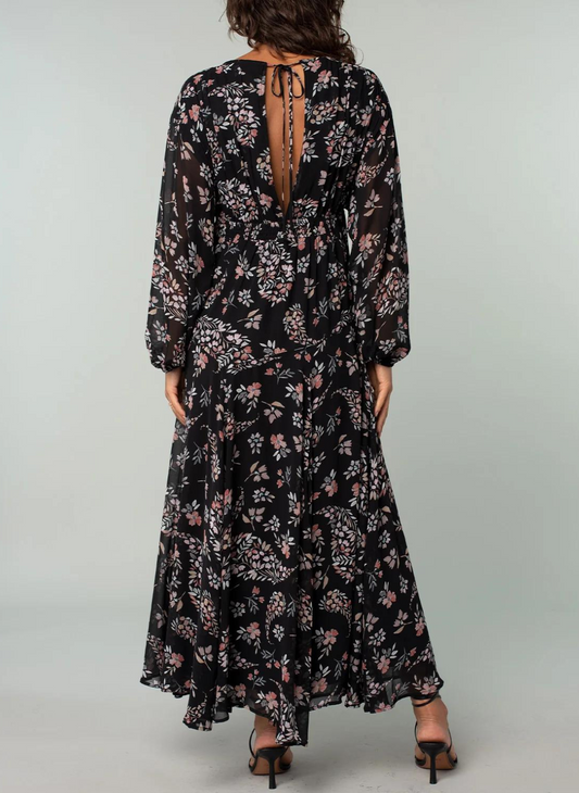 Model is showing the back of the floral dress, where there is a V-neck with a string tie on top.