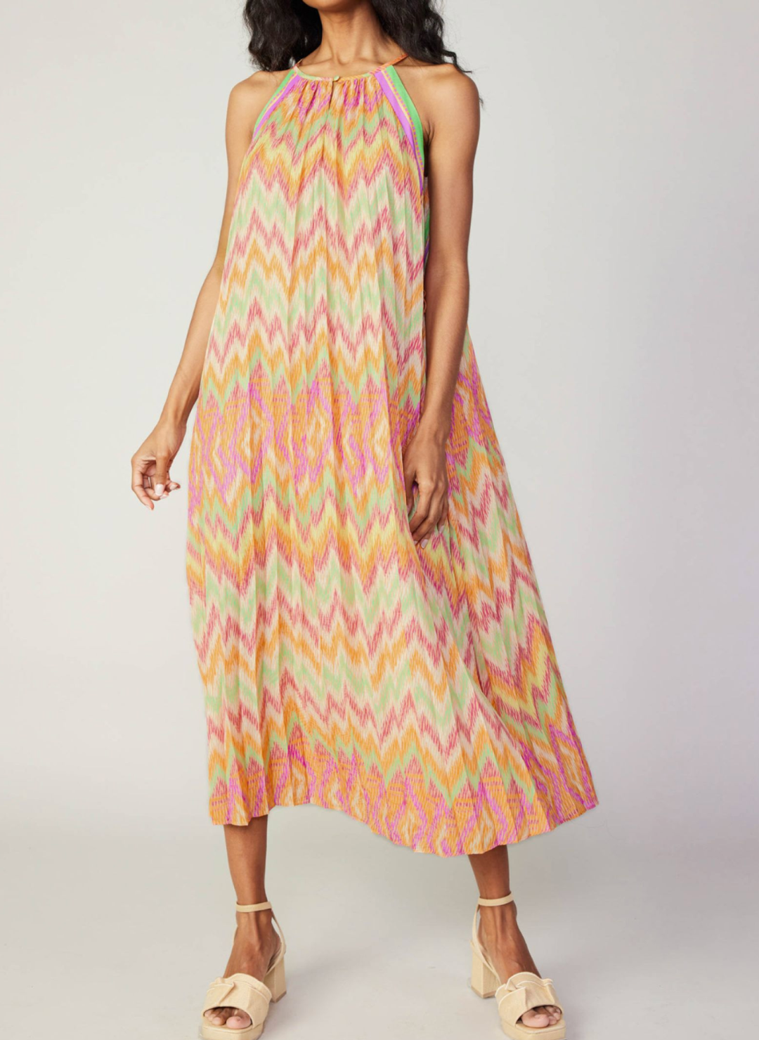Model wearing colorful chevron pleated dress with high neckline and no belt tie.