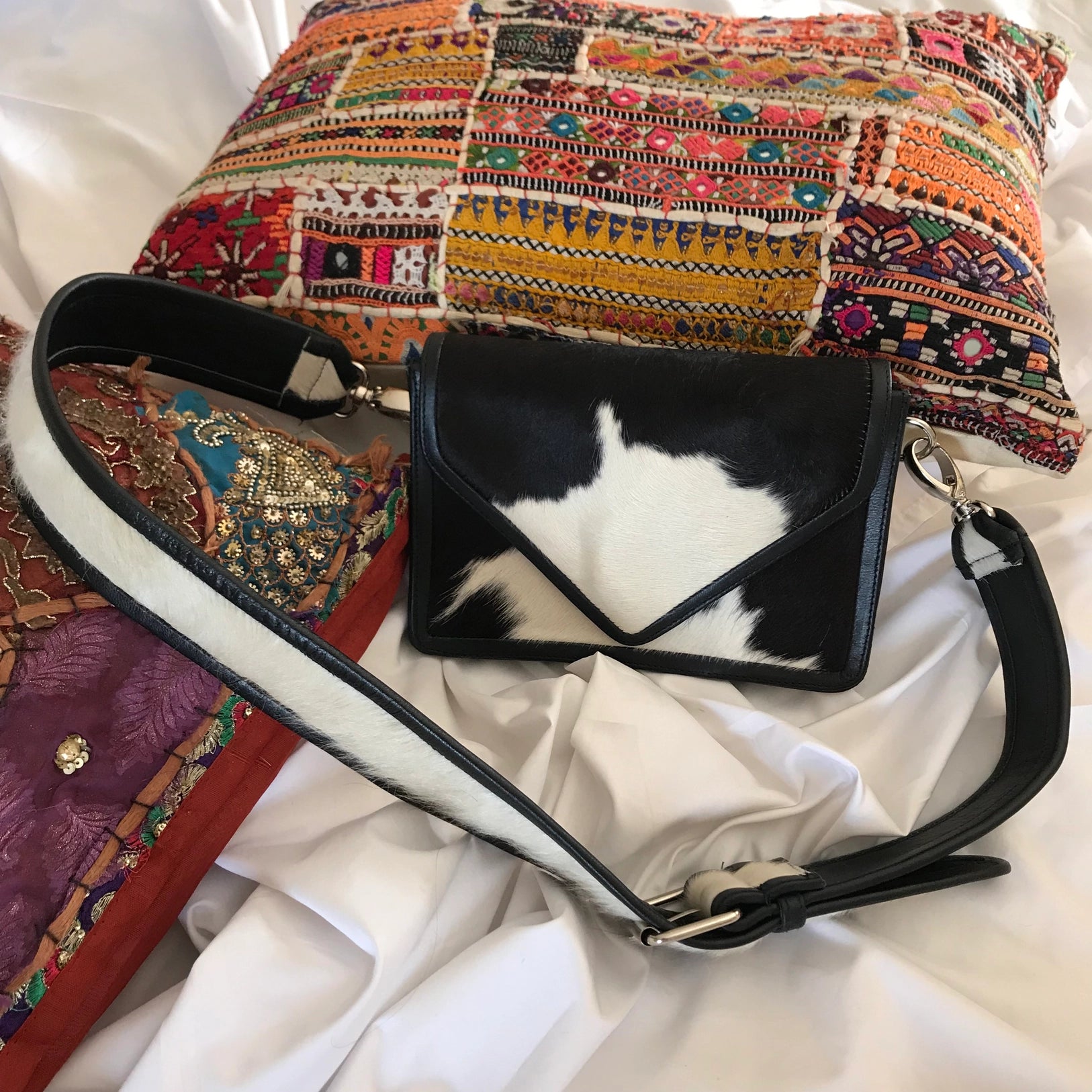 Front view of the cow purse and attached strap sitting up on a embroidered pillow.