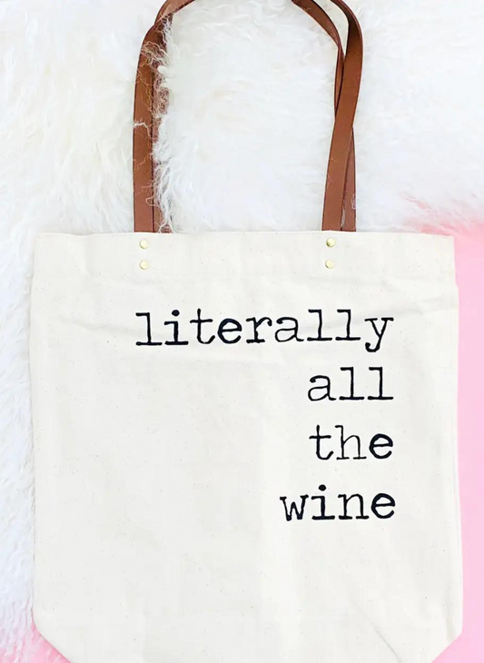 Image shows a tote bag with a faux leather handle. With “ literally all the wine” printed on the bag.