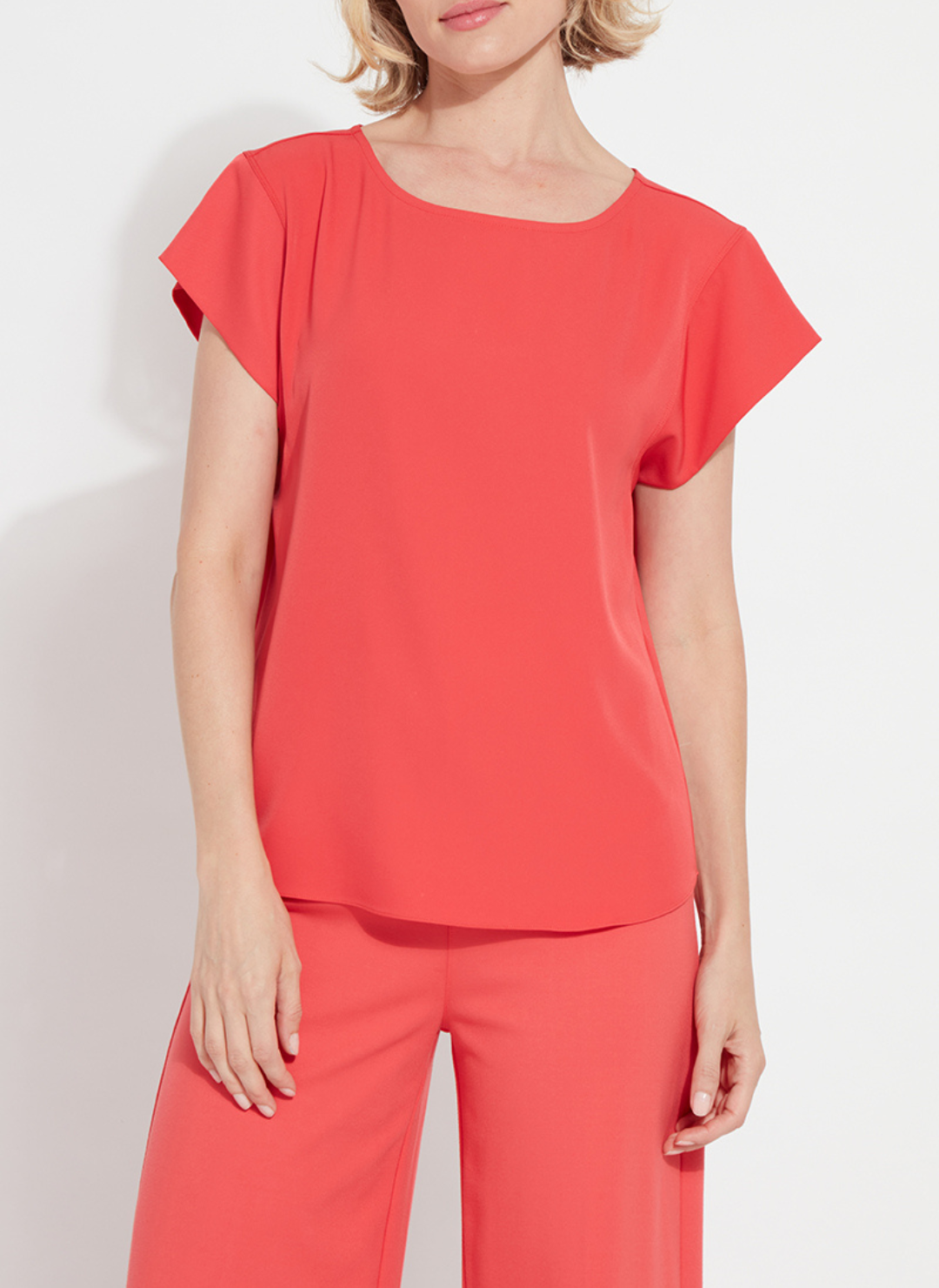 Woman wearing the Melodie Top in Coral Bloom from August Boutique Ripon; features flutter sleeves, scoop neckline, flowy drape, and keyhole back detail. Lightweight and perfect for warm-weather styling.