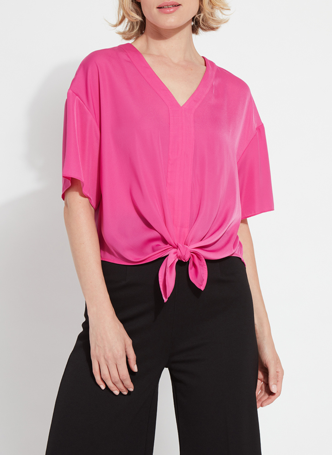 Woman wearing the Lyssé Cleo Tie Up Top in vibrant hot pink; features dolman short sleeves, v-neckline, and tie-front hem. Styled for comfort and polish, available at August Boutique Ripon.