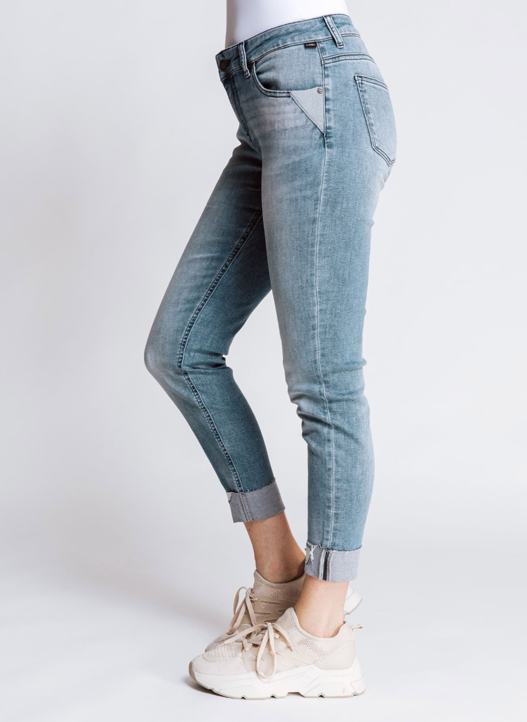 Side view of model wearing ZHRILL Nova Jean with denim pants and beige shoes. White background.