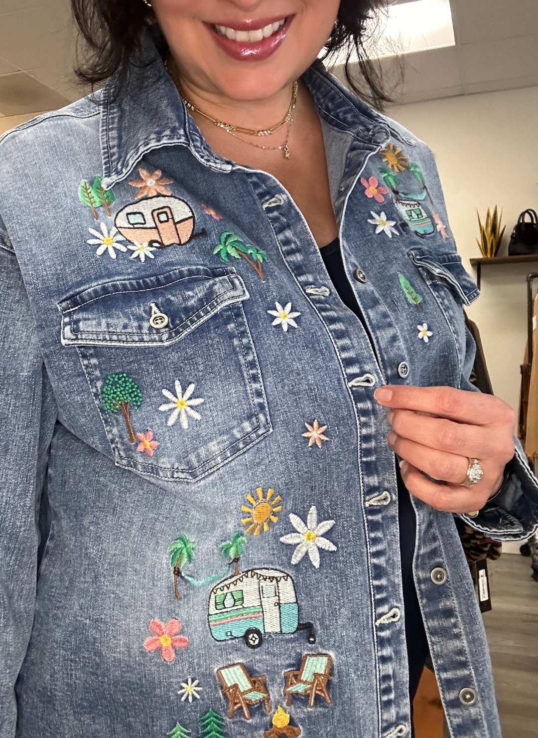 Up close view of model wearing denim camper shirt with embroidered flowers, trees, and trailers.