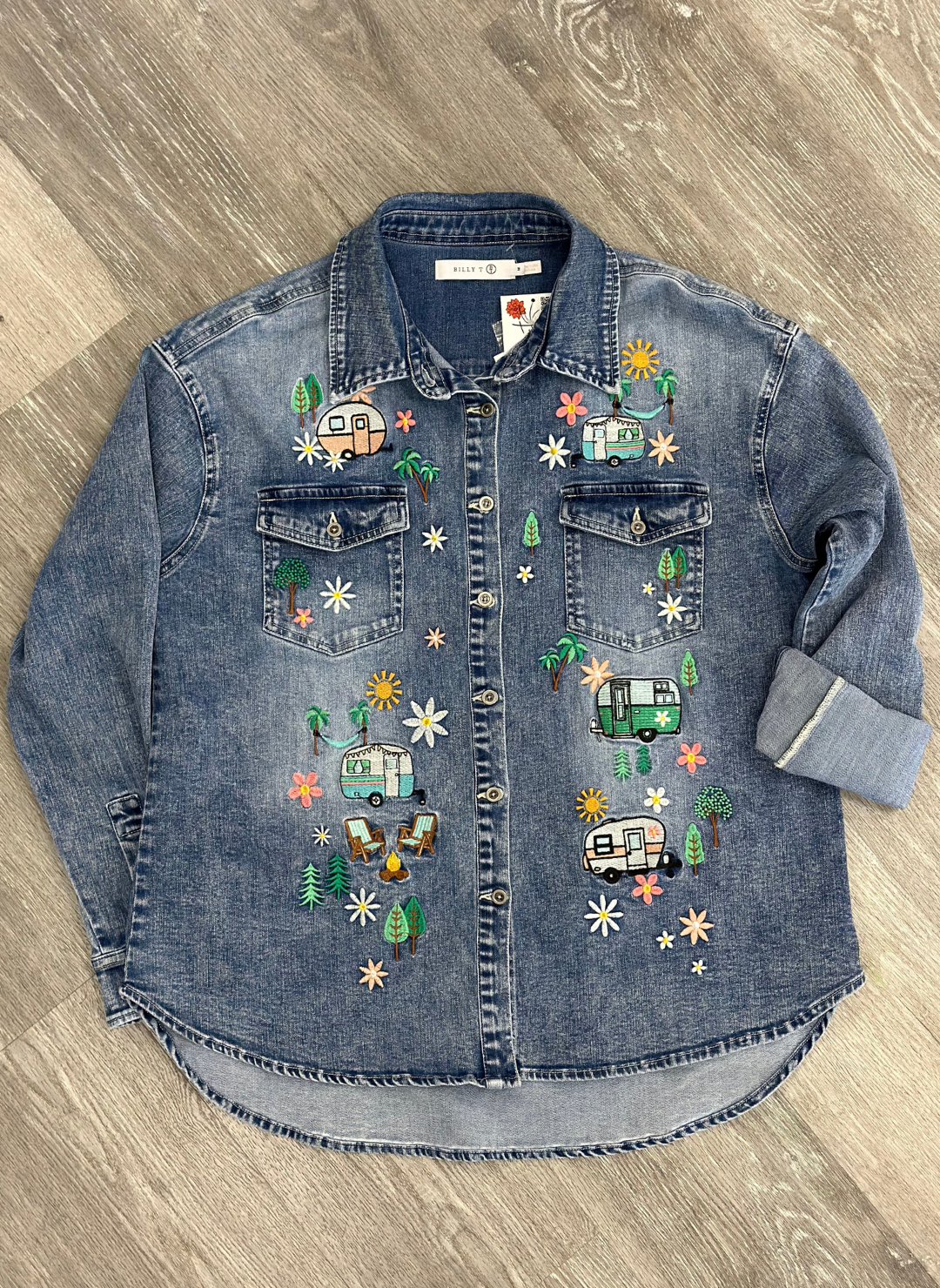 Flat image of denim camper shirt with embroidered flowers, trees, and trailers.
